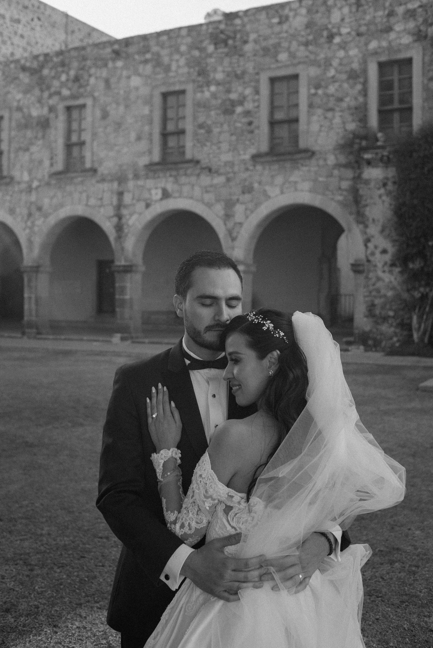 An intimate black and white portrait showcasing a tender moment against historic stone architecture.