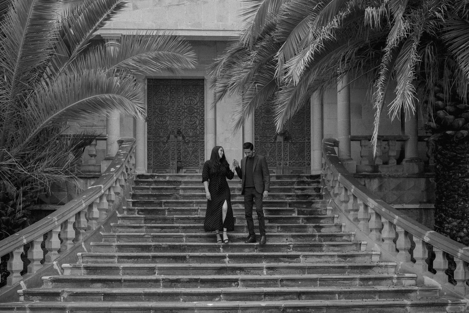 Black and white photo of couple ascending grand stone steps with palm trees.