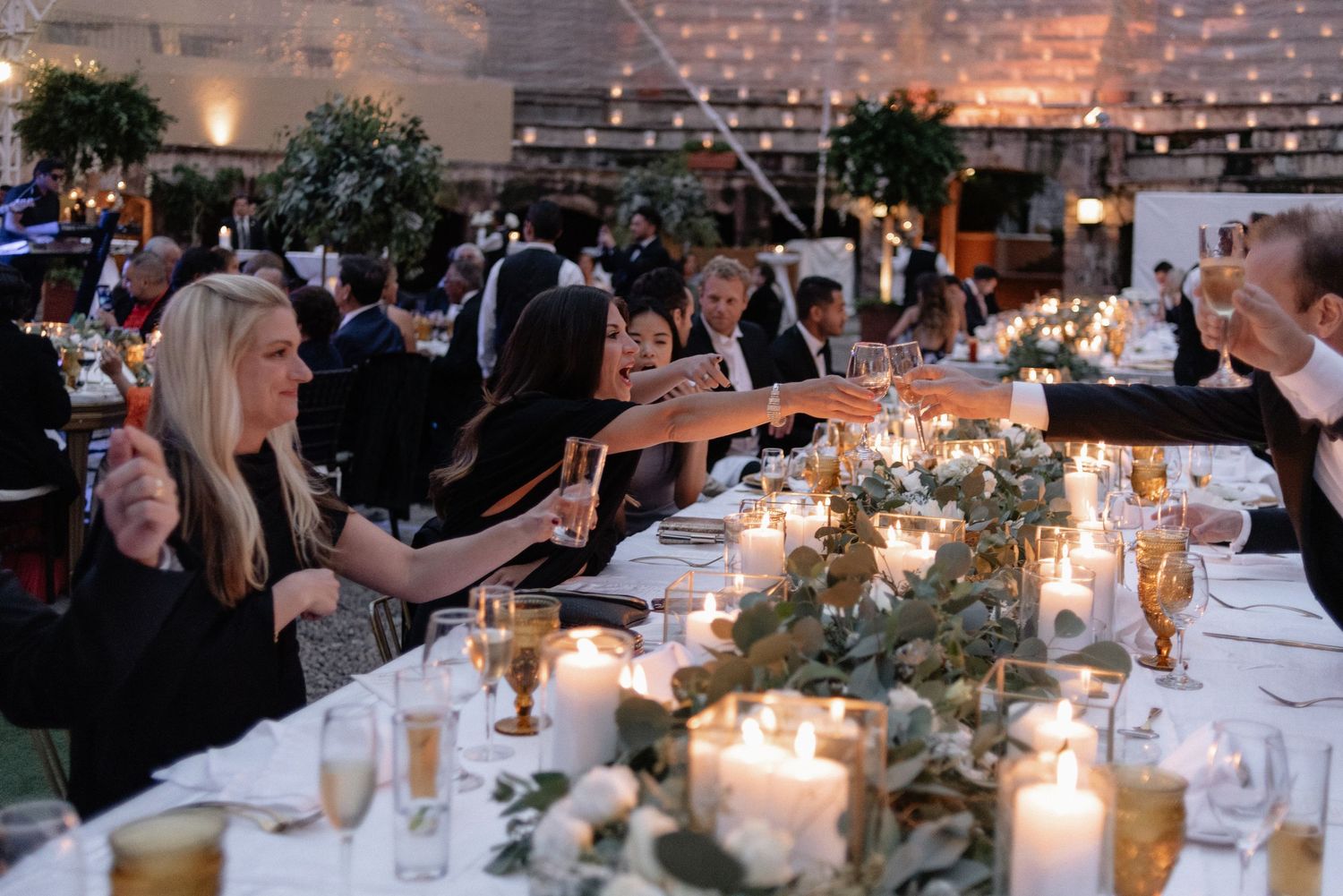 Candlelit wedding reception table glows warmly with floral centerpieces and glassware in an intimate indoor setting.