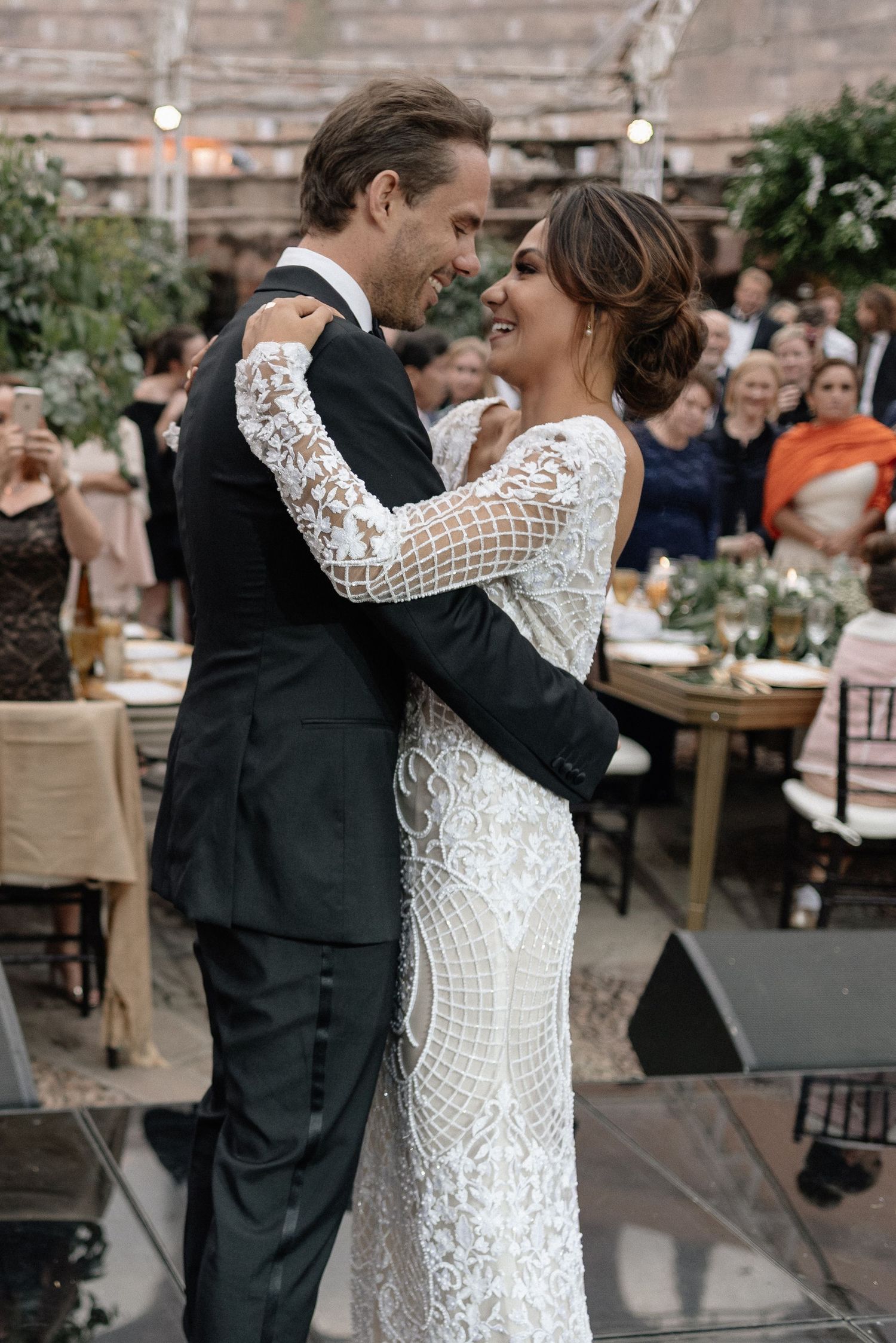 Newlywed couple shares their first dance at an outdoor wedding reception under string lights and surrounded by guests.