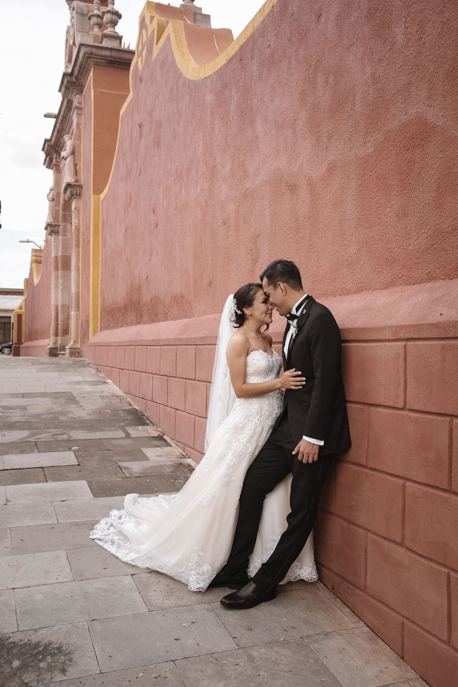 A romantic wedding moment against a terracotta wall at a historic venue.