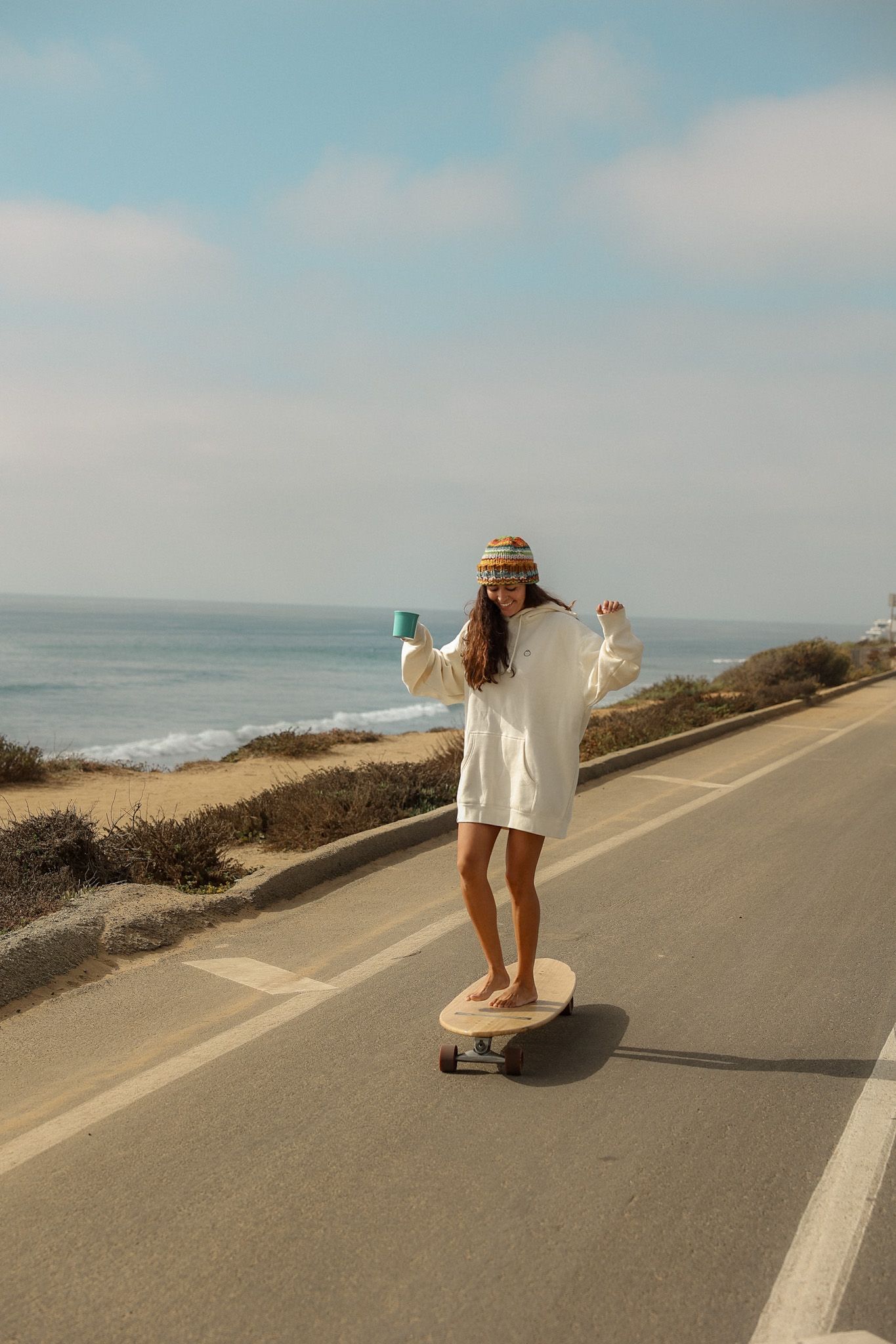 Girl wearing a white Sunbum Jacket, enjoying a partly sunny day while skateboarding with a carefree vibe, promoting Sunbum sunscreen.