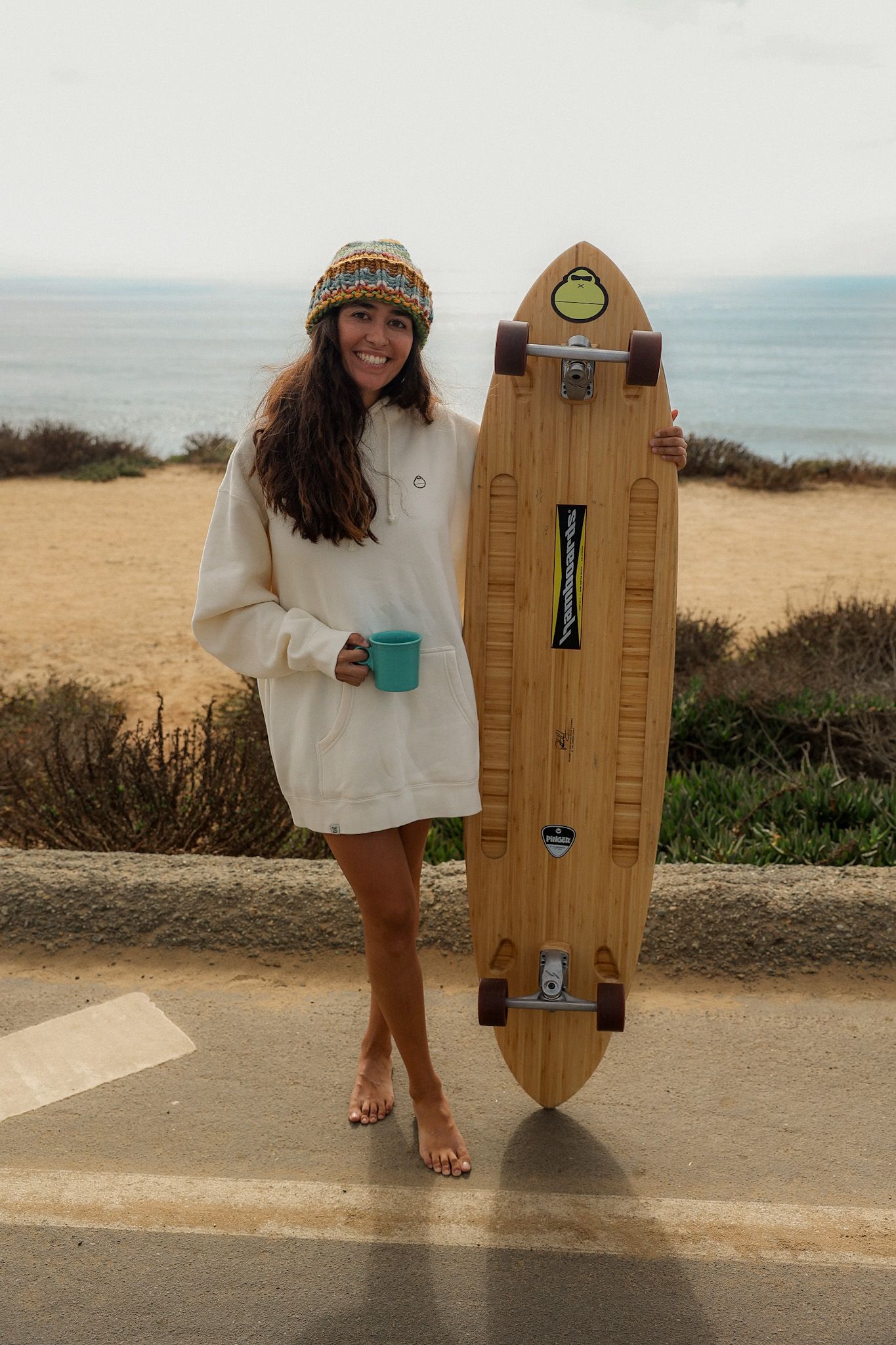 Girl wearing a white Sunbum Jacket, enjoying a partly sunny day while standing with a skateboard, promoting Sunbum sunscreen.