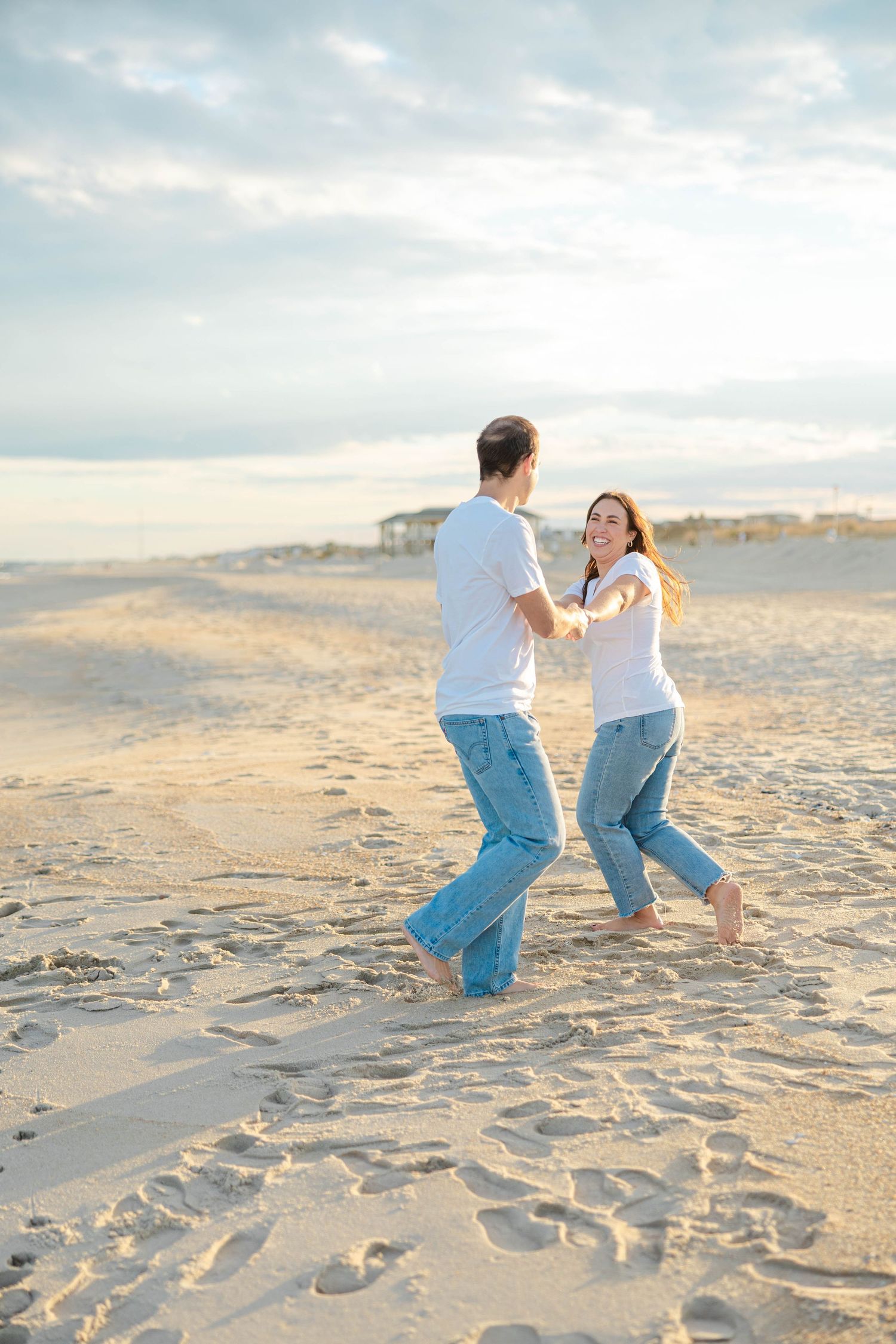 Two people in matching blue jeans dance together on a sandy beach at sunset.