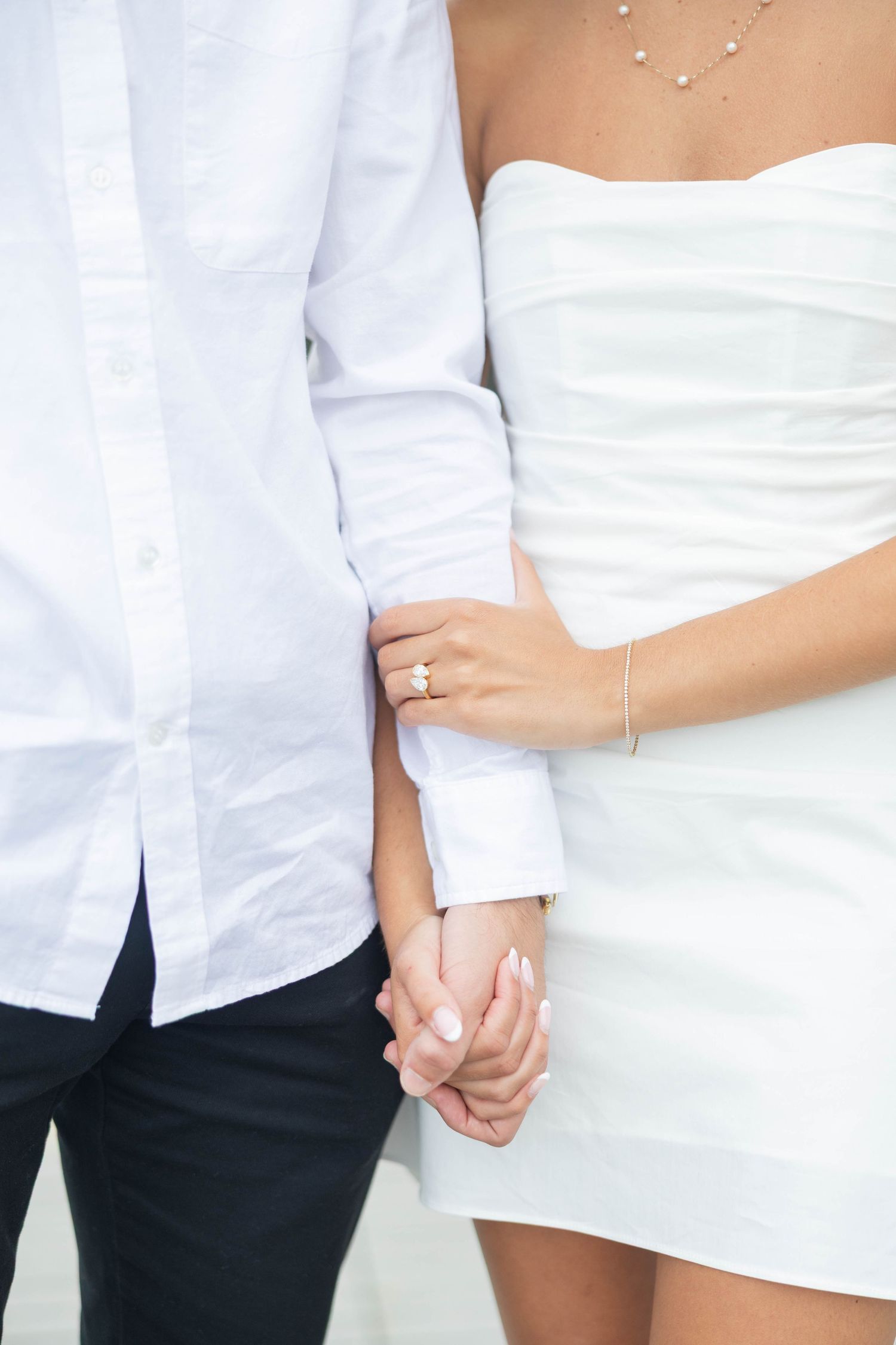 Close-up photo showing couple holding hands, wearing white and black casual clothing against a white background.