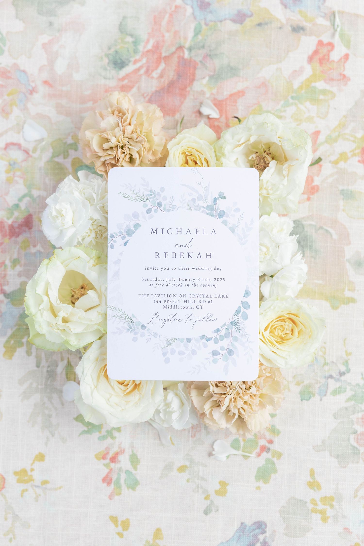 Elegant wedding place cards with calligraphy names displayed among soft white and cream roses on a pastel floral background.