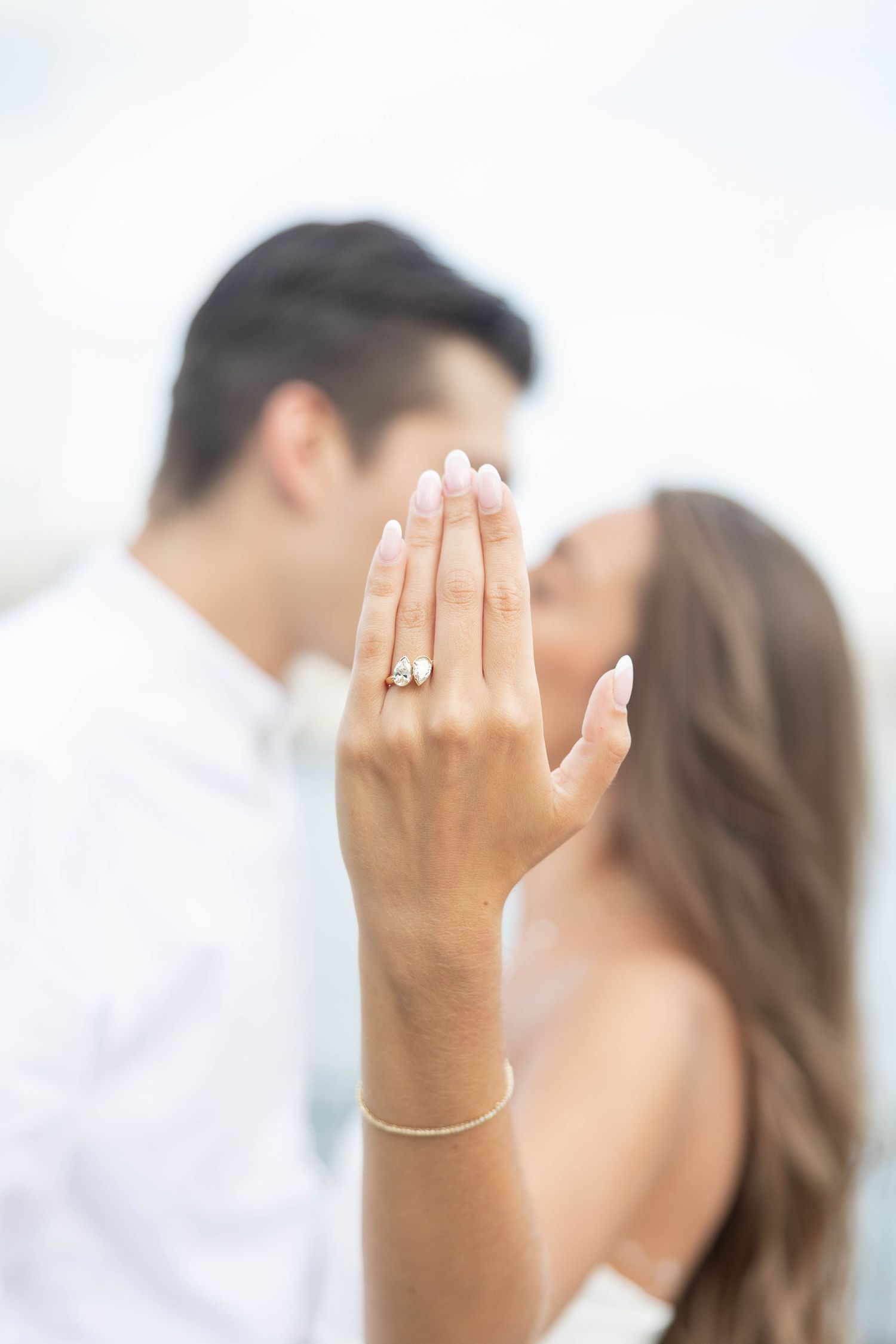A close up shot of a woman's hand with an engagement ring and bracelet against a soft blurred background.