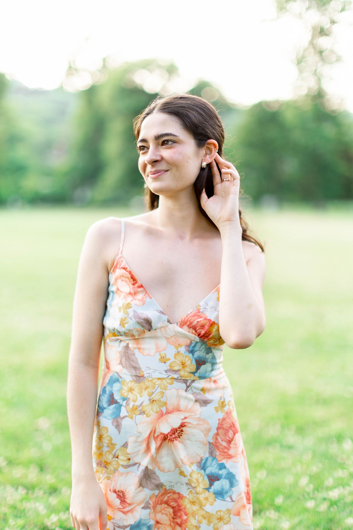 Portrait of someone in a floral dress touching their hair in a sunny field.