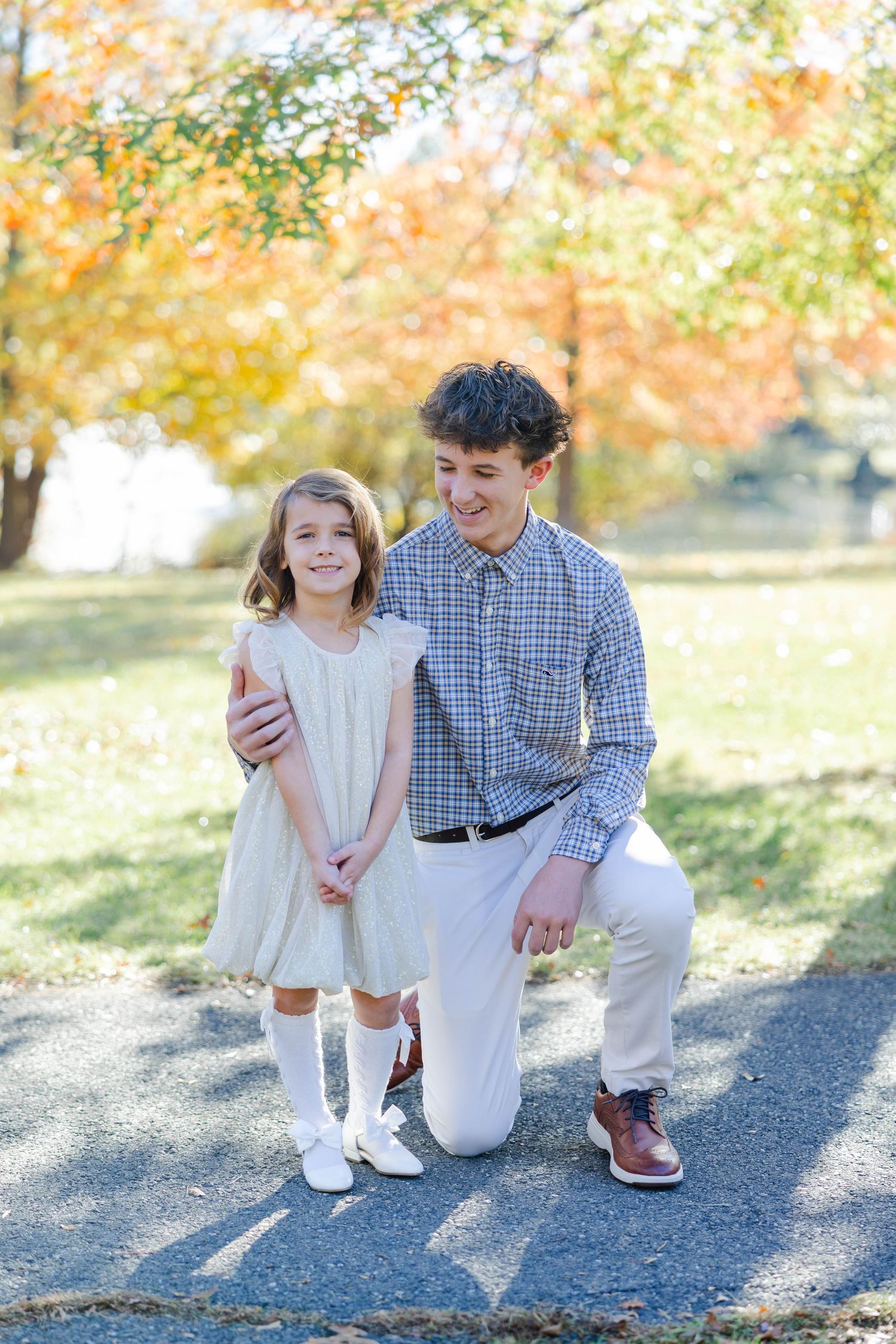 Parent and child share tender moments outdoors during autumn photoshoot with golden sunlight and falling leaves.