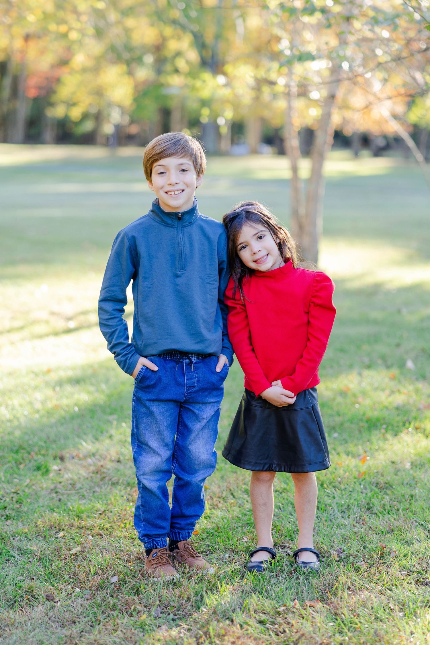 Two children in blue and red outfits playing together outdoors on grass during autumn.