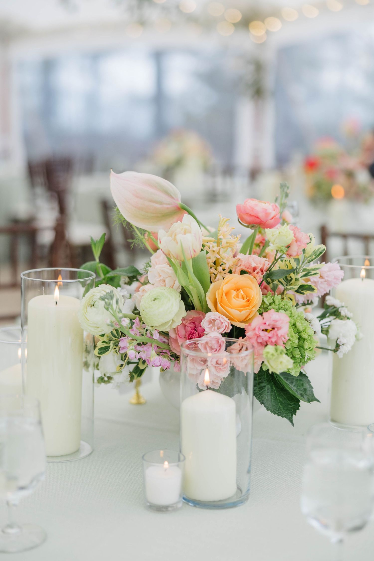 Elegant wedding centerpiece with pastel flowers, tulips, ranunculus, and white pillar candles on a light tablecloth.