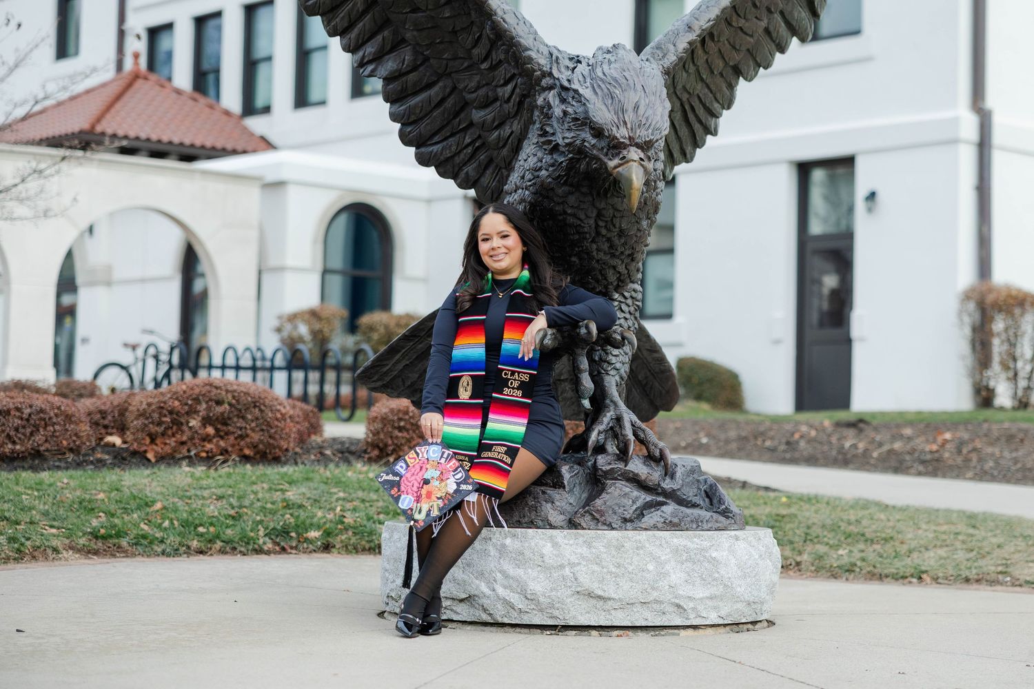A large bronze eagle sculpture with spread wings stands prominently on a stone pedestal near a building.