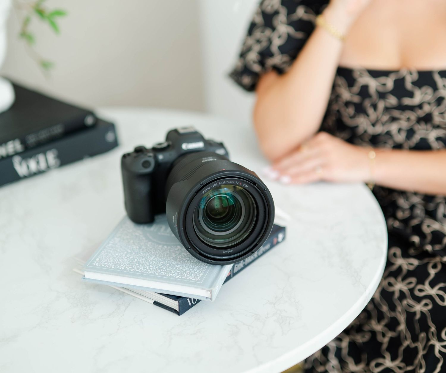 Professional camera with lens resting on white surface next to black patterned fabric.