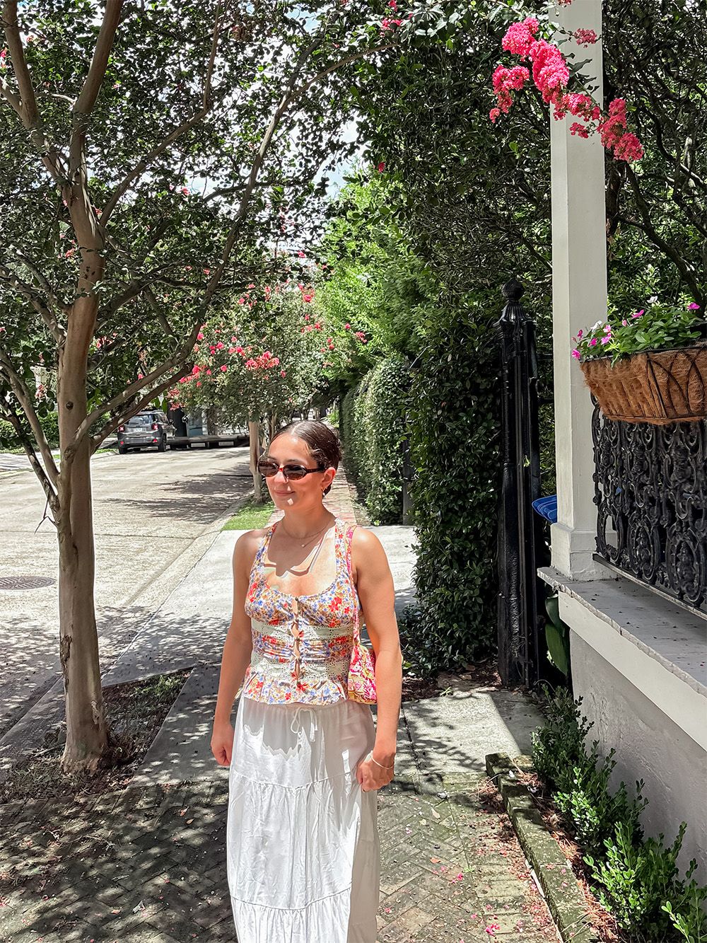 Summer street scene with lovely pink bougainvillea flowers climbing white column and trees lining a sunny sidewalk.