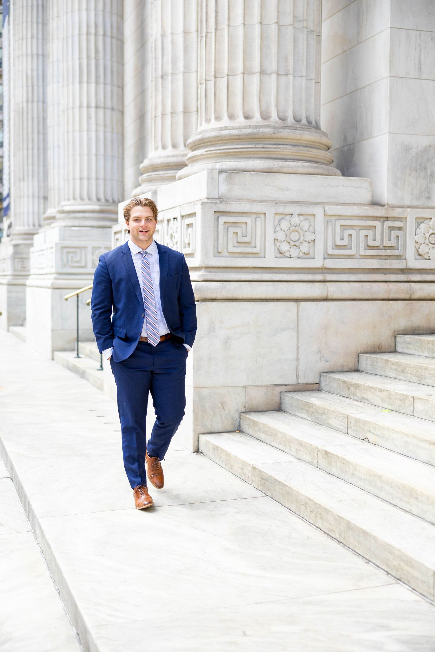 Professional in navy suit descends marble steps of classical building with columns.