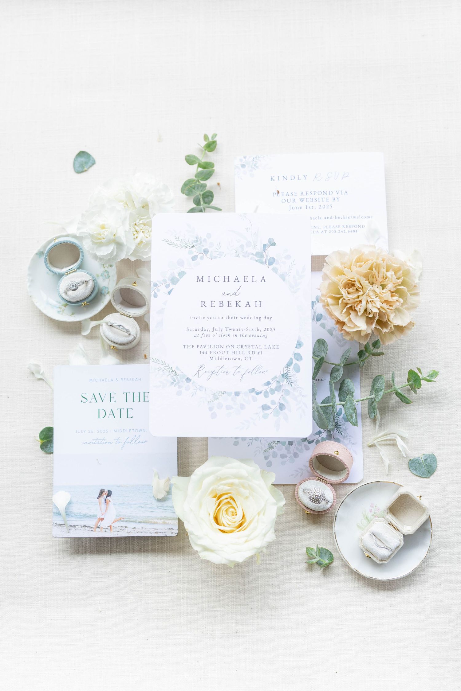 Elegant wedding invitations and save the date cards displayed with floral arrangements, tea cups, and eucalyptus leaves on white.