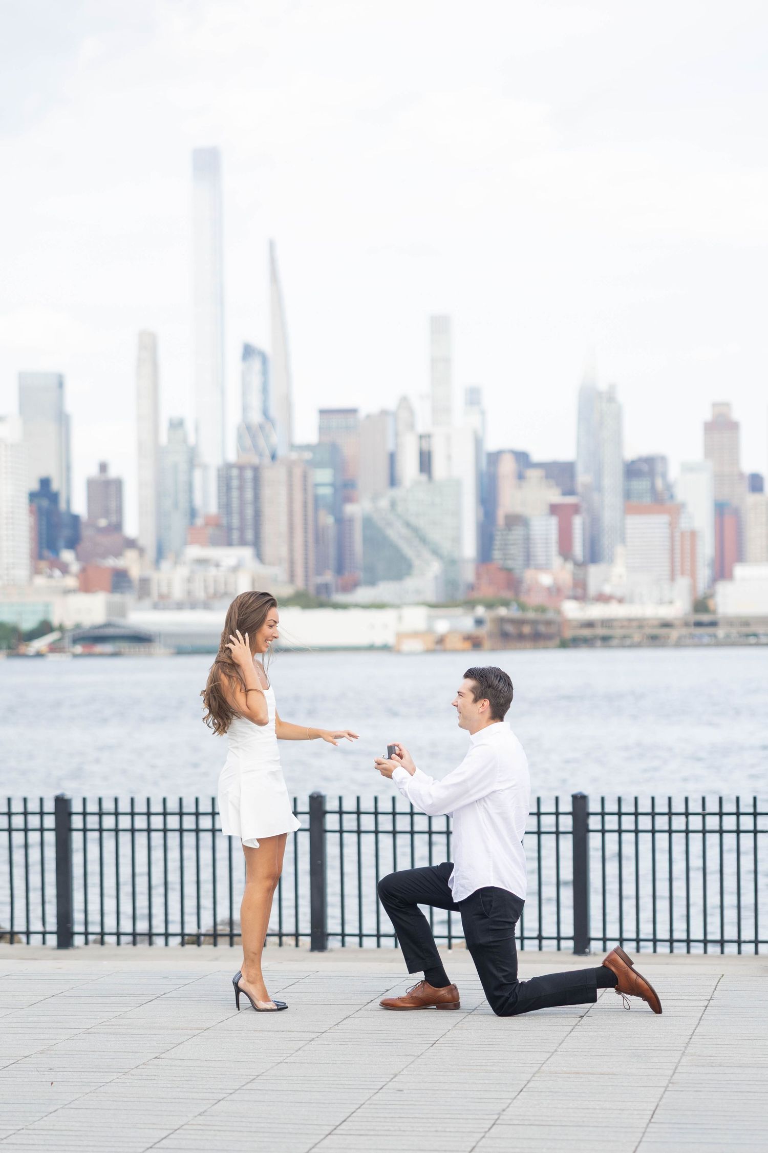 A romantic marriage proposal sequence on a waterfront promenade with the Manhattan skyline in the background.