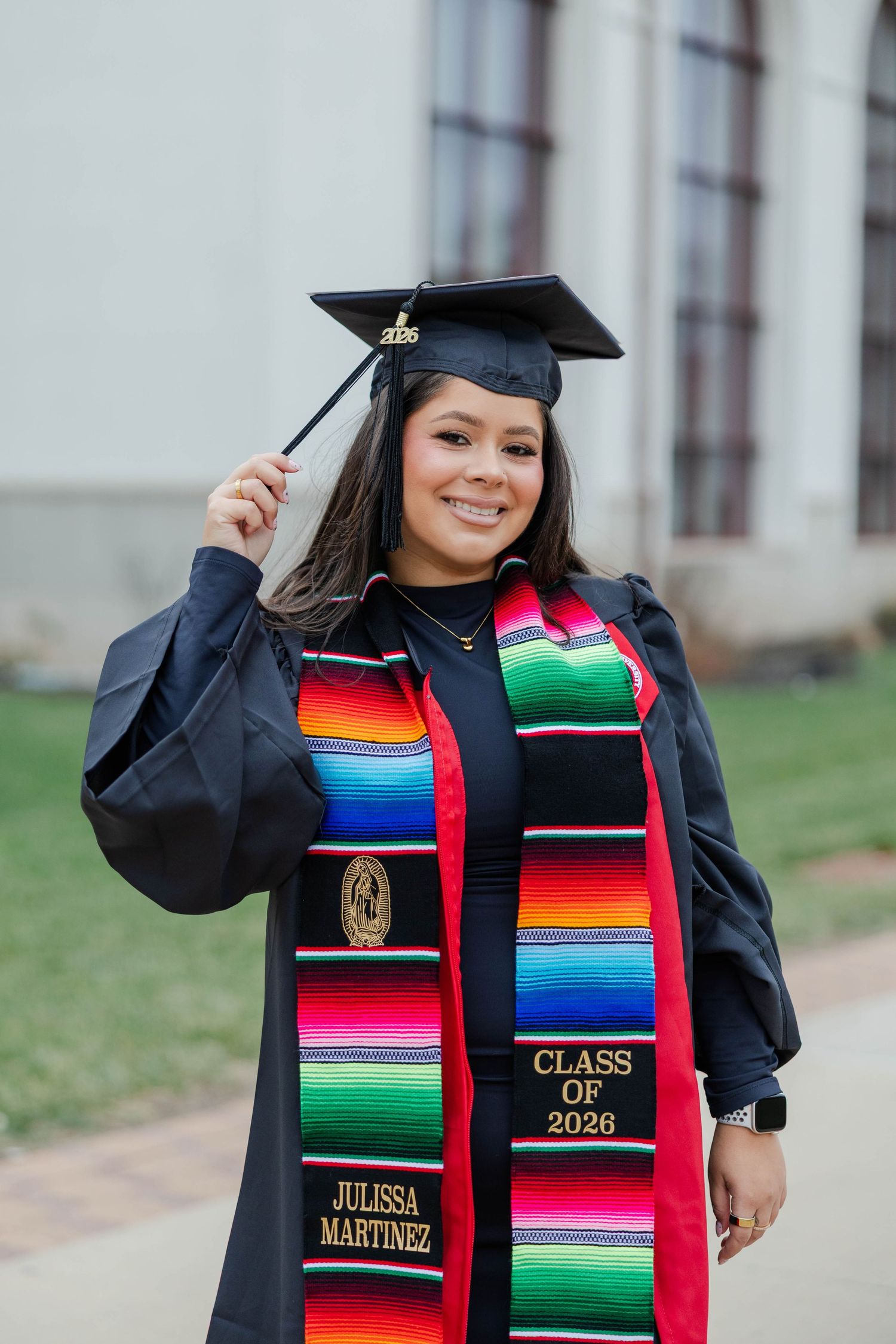 Graduate wearing colorful Mexican serape stole and black cap and gown poses for graduation photos.