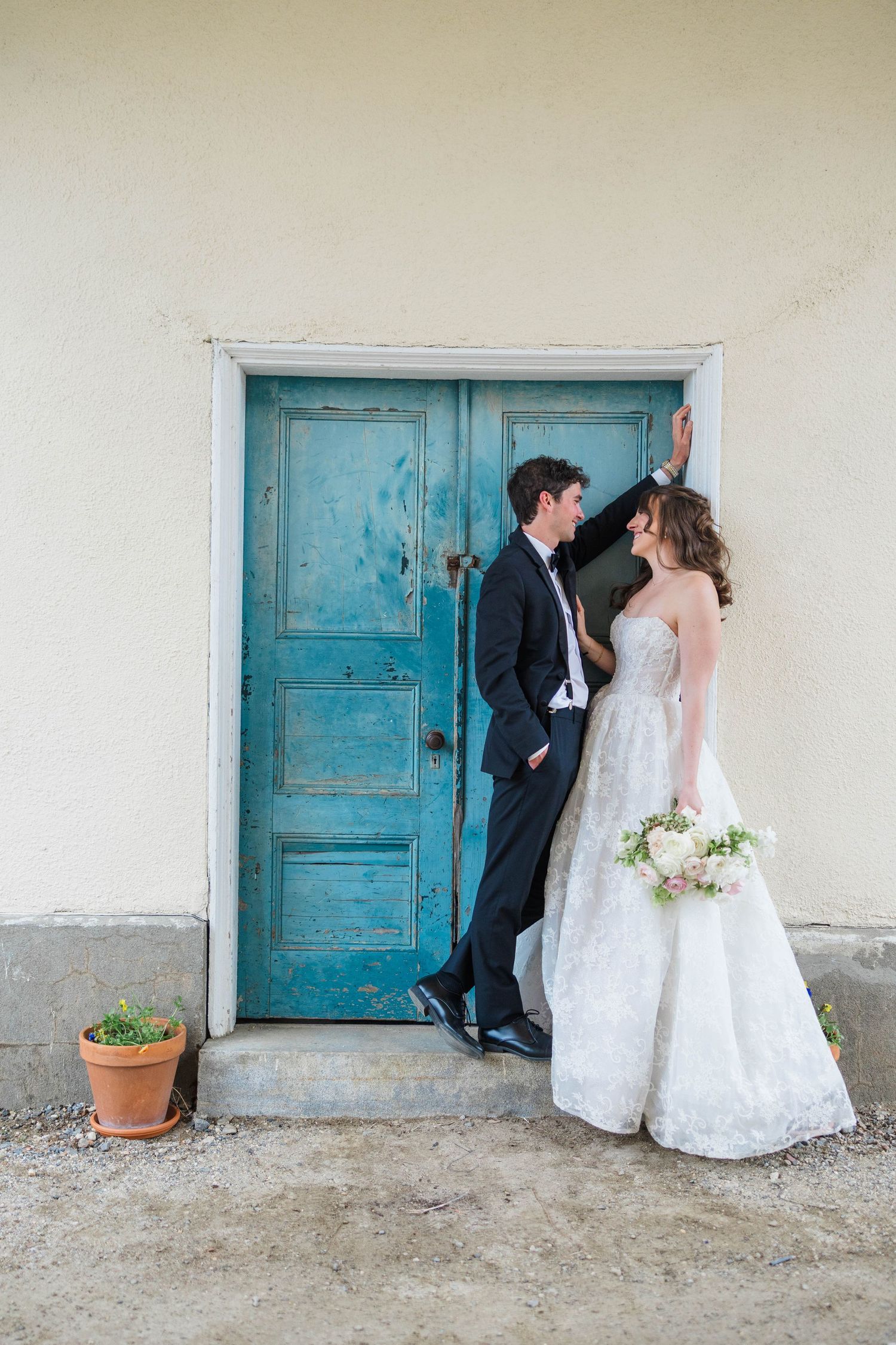 Bride and groom posing by a rustic turquoise door, bride holding a bouquet in a strapless lace gown.