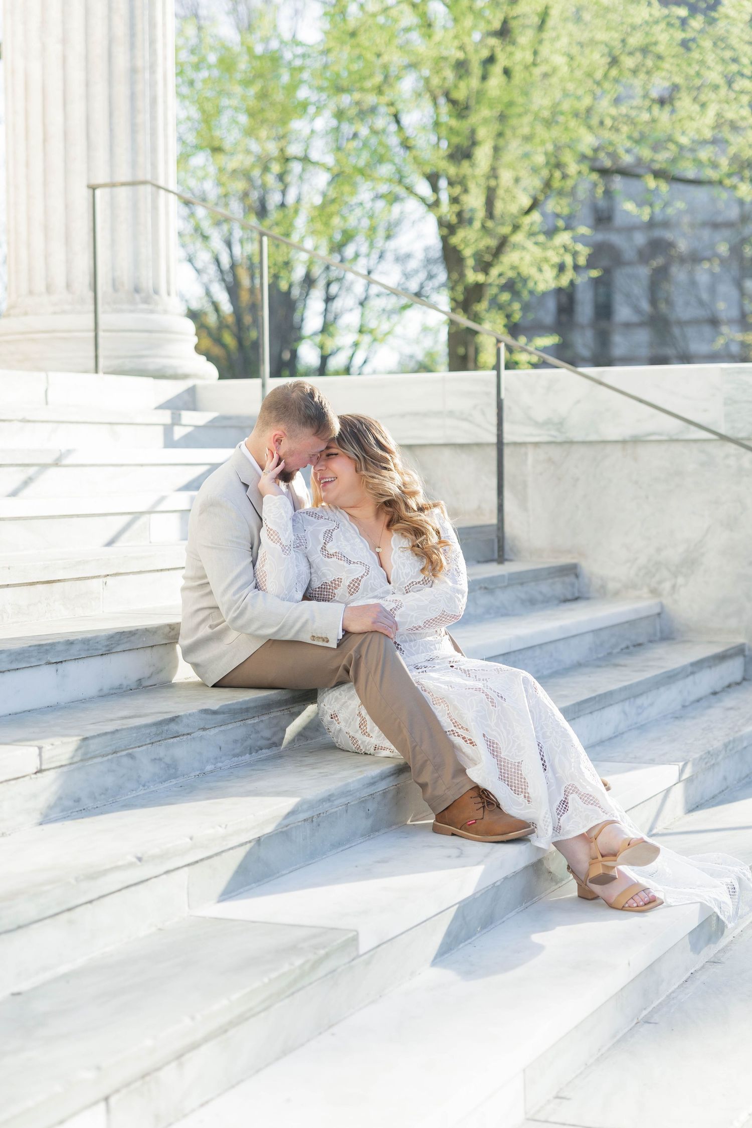 Couple sitting closely together on marble steps, sharing a romantic moment in soft natural light.