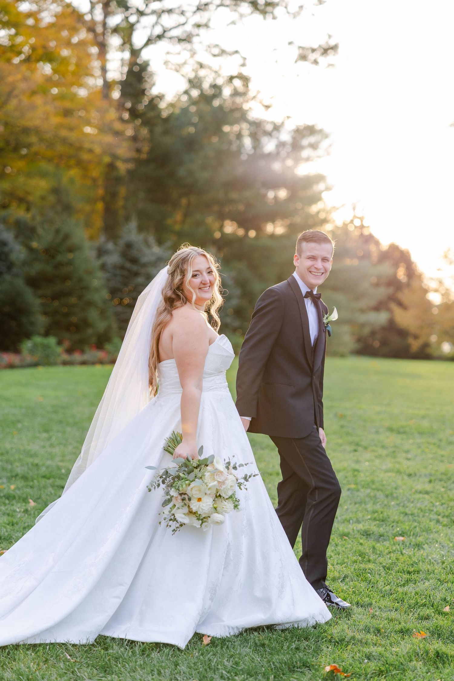 A joyful wedding party celebrates on a grassy hill at sunset during an autumn outdoor wedding ceremony.