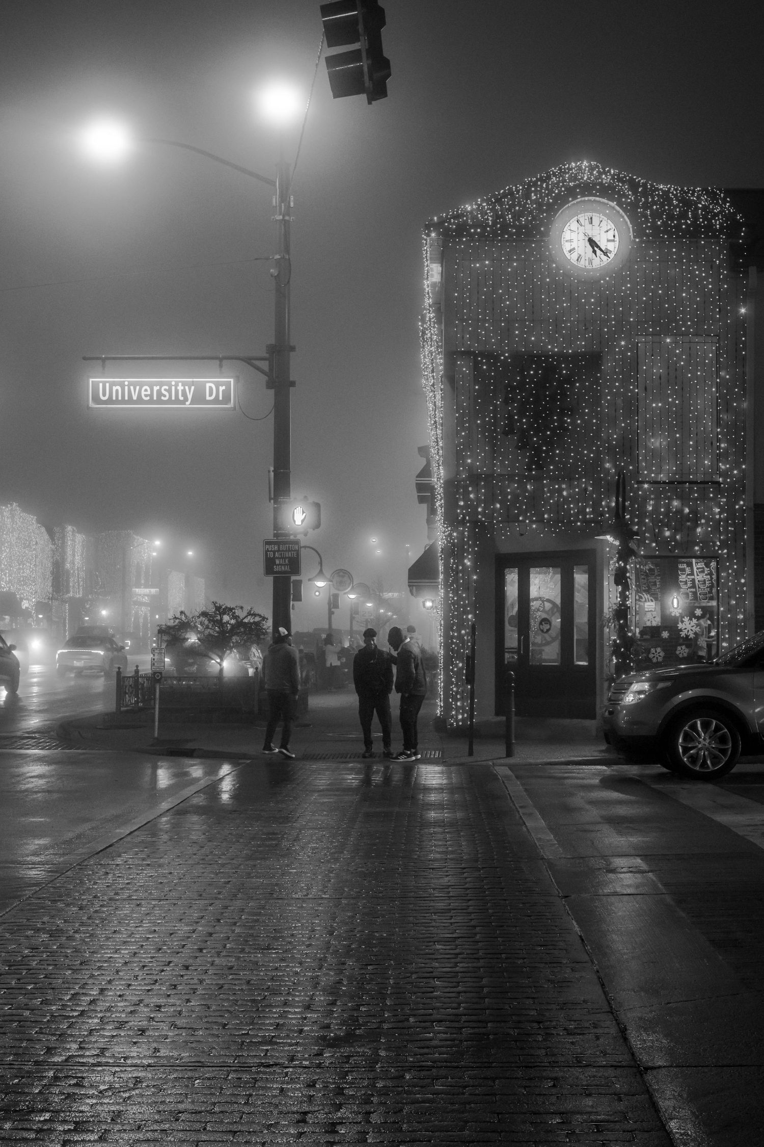 A foggy night street scene with illuminated clock tower building and University street sign.