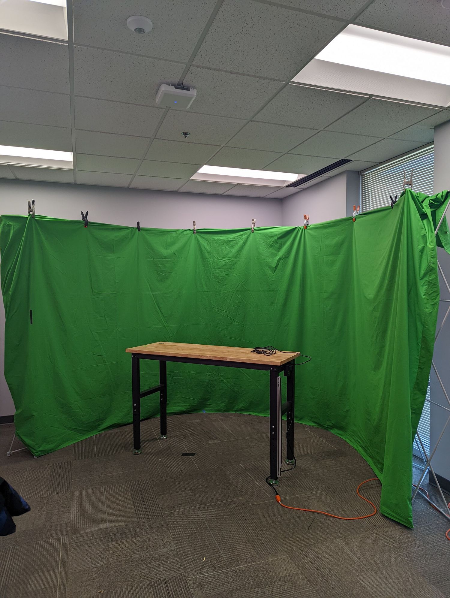 Green screen setup in office space with wooden table and fluorescent lighting.