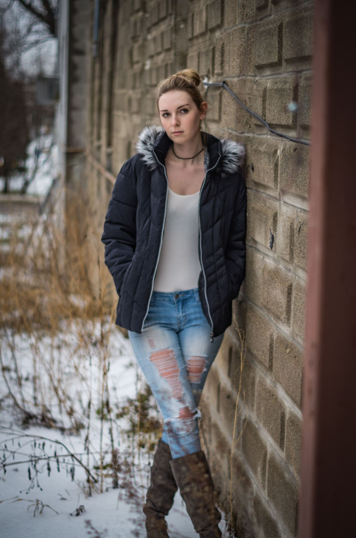 Winter portrait against brick wall featuring casual outfit with puffy jacket and ripped jeans.