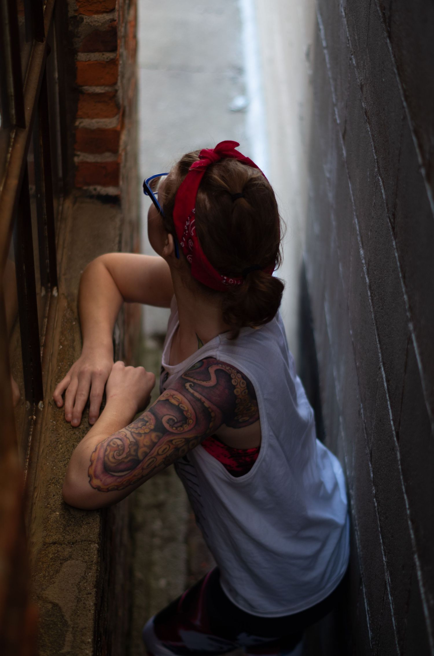 Side view of person with tattoo and red bandana leaning against brick wall.