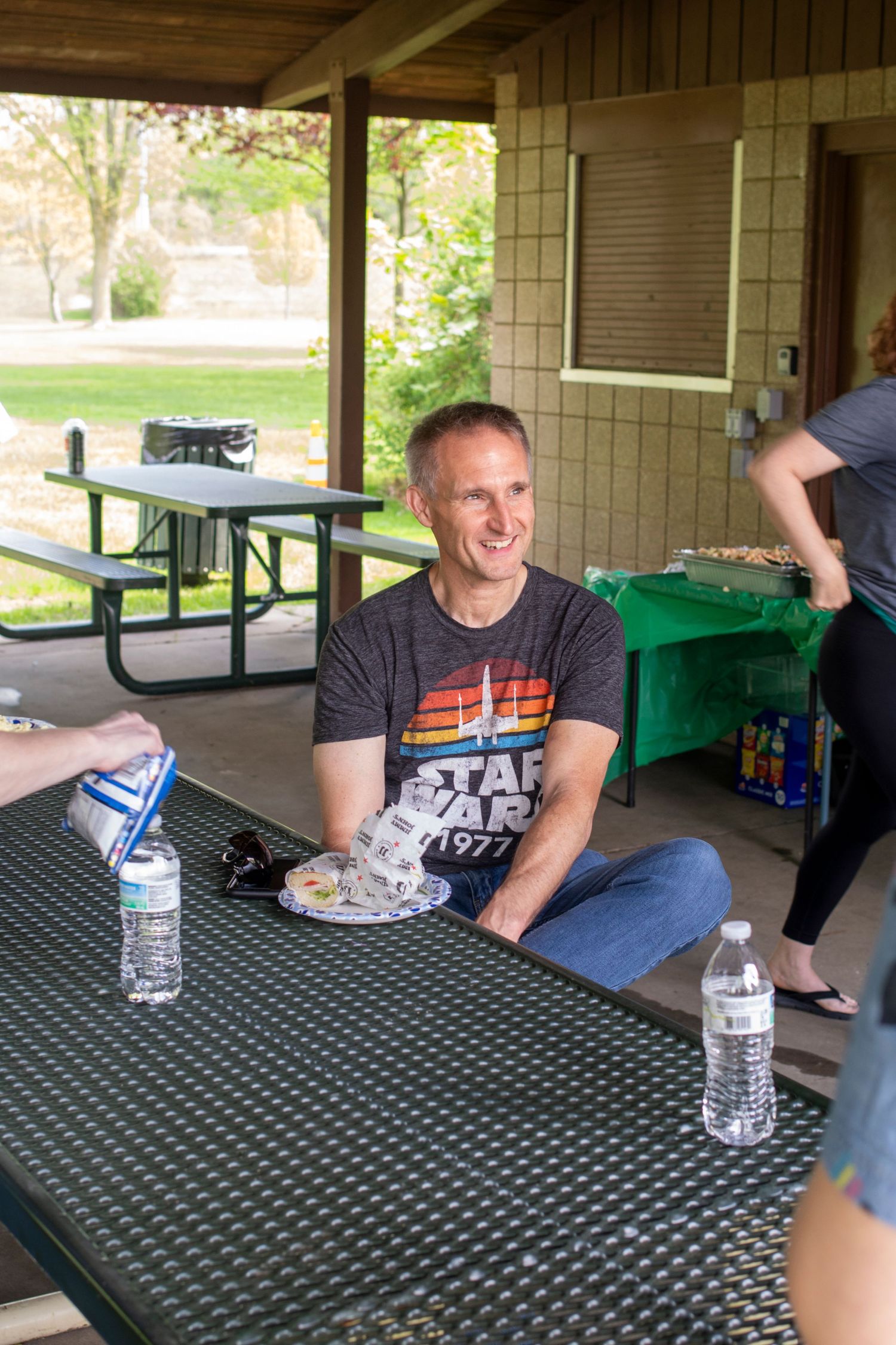 Person sitting at picnic table under covered porch area with water bottles.