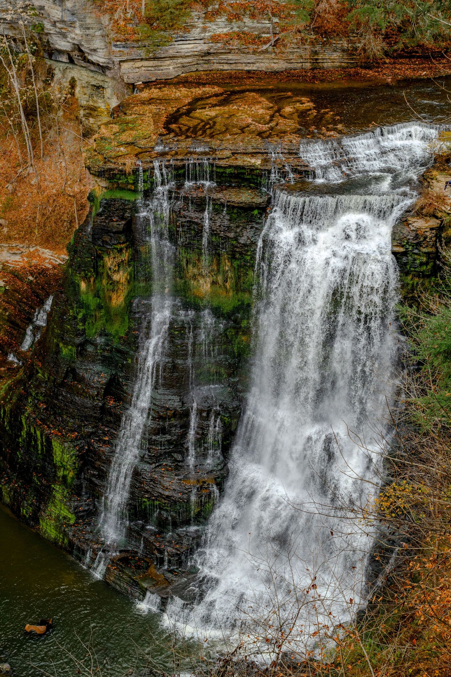 Majestic waterfall cascading down moss-covered rock face surrounded by fall colors.