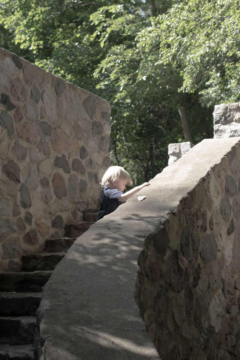 Stone stairway curving around wall with dappled sunlight through trees.