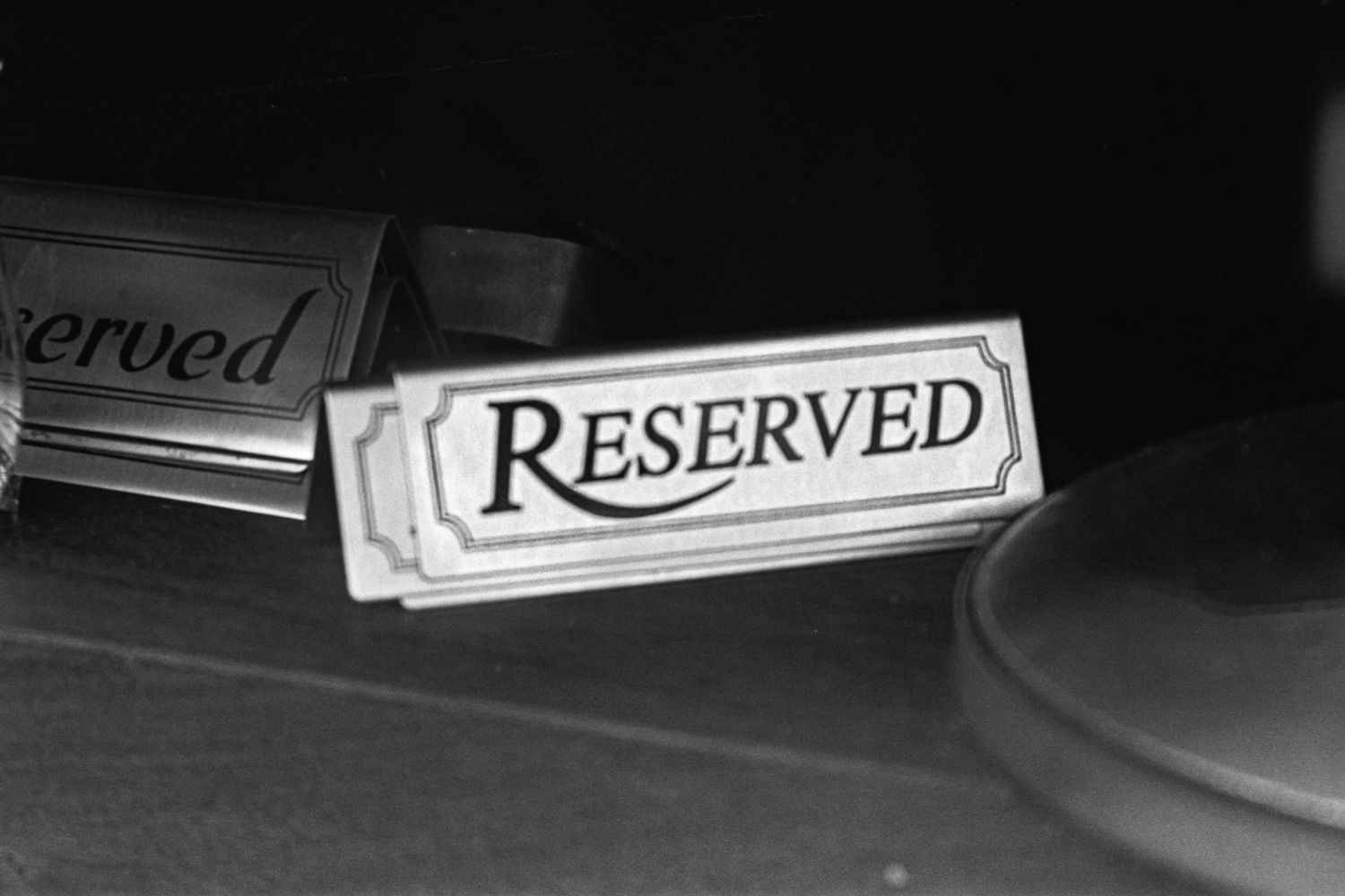 A black and white close-up of a reserved table sign in low lighting.
