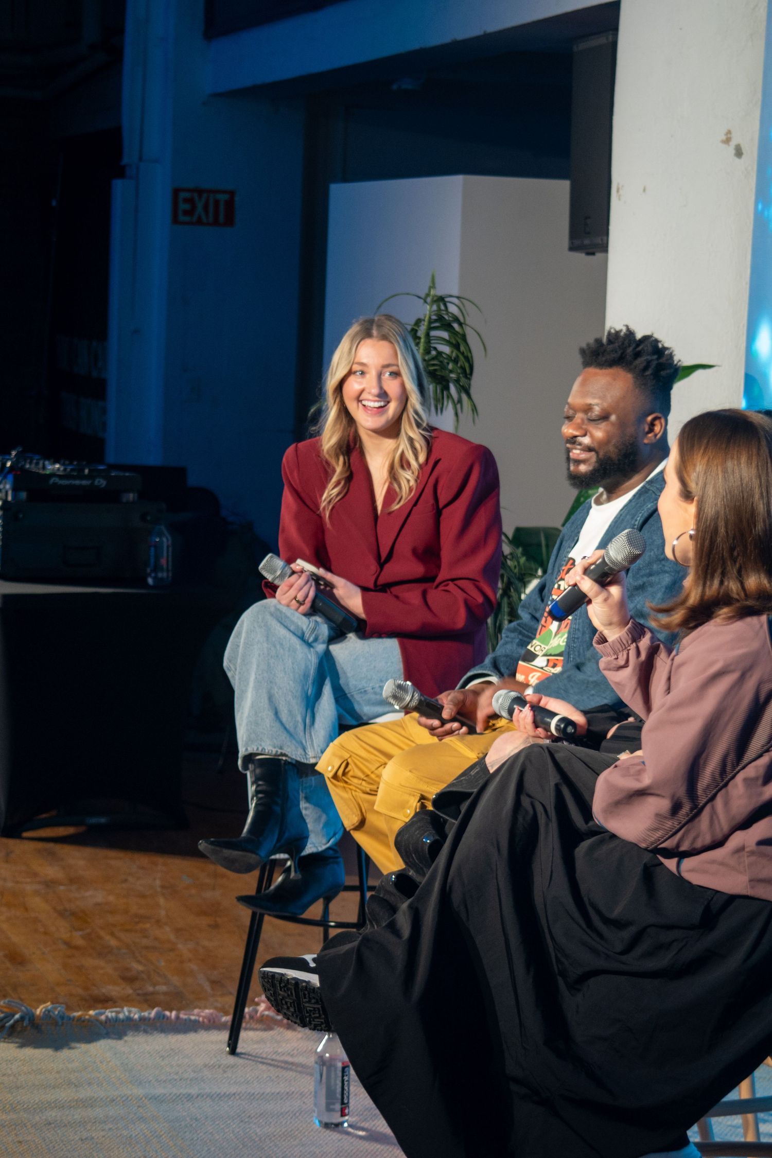 A group of people sitting in chairs having an animated conversation in a dimly lit room.