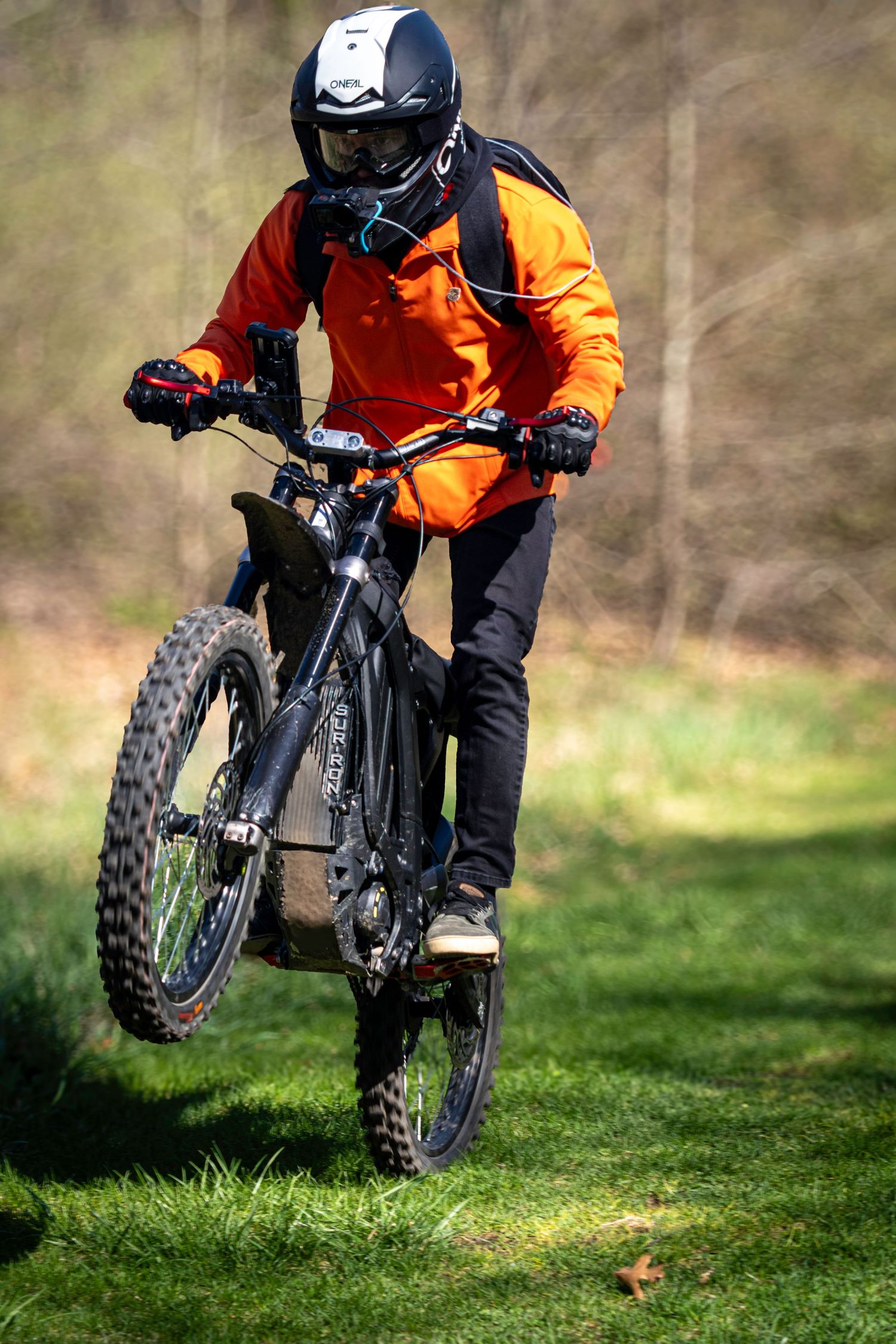Mountain biker performing small jump on grassy terrain in protective gear.