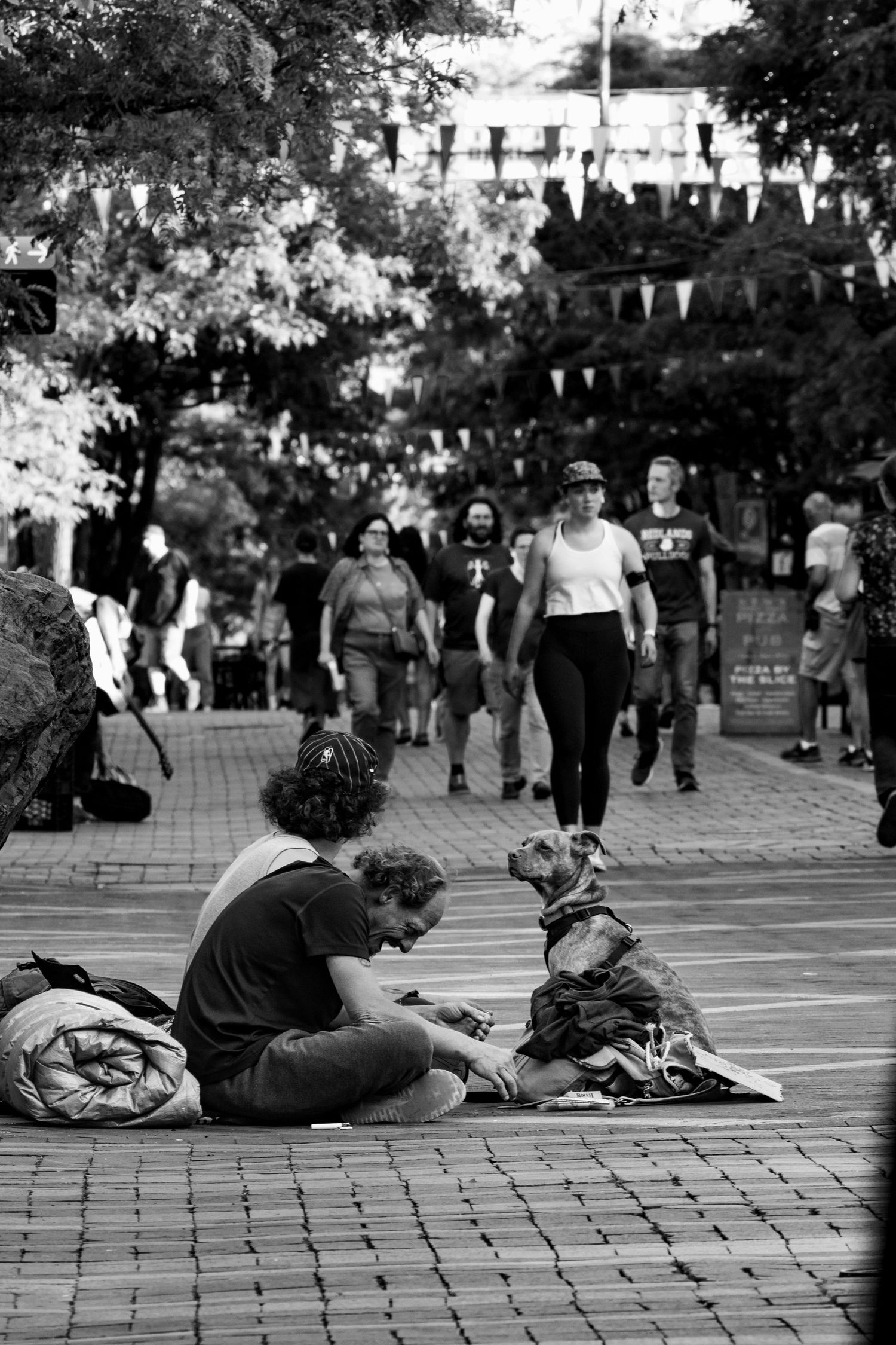 Black and white street scene showing people on brick pavement with festival bunting hanging overhead.