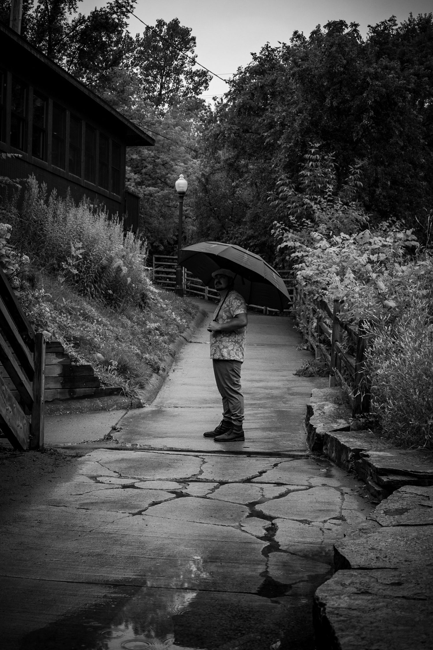 Figure with umbrella standing on wet stone path in black and white.