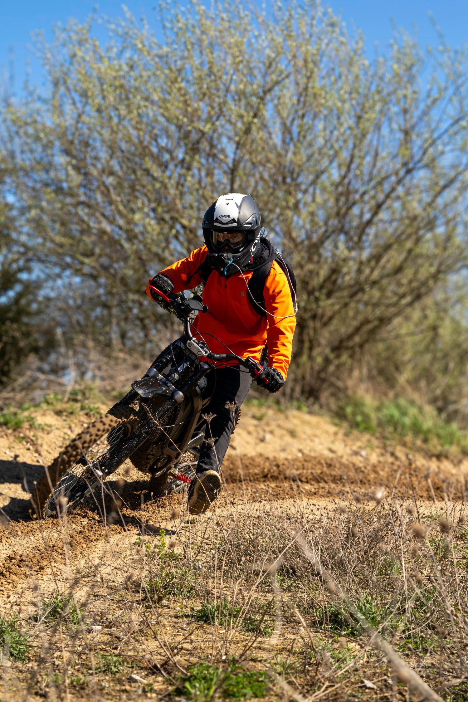 Off-road motorcyclist maneuvering through dirt trail in bright orange protective gear.