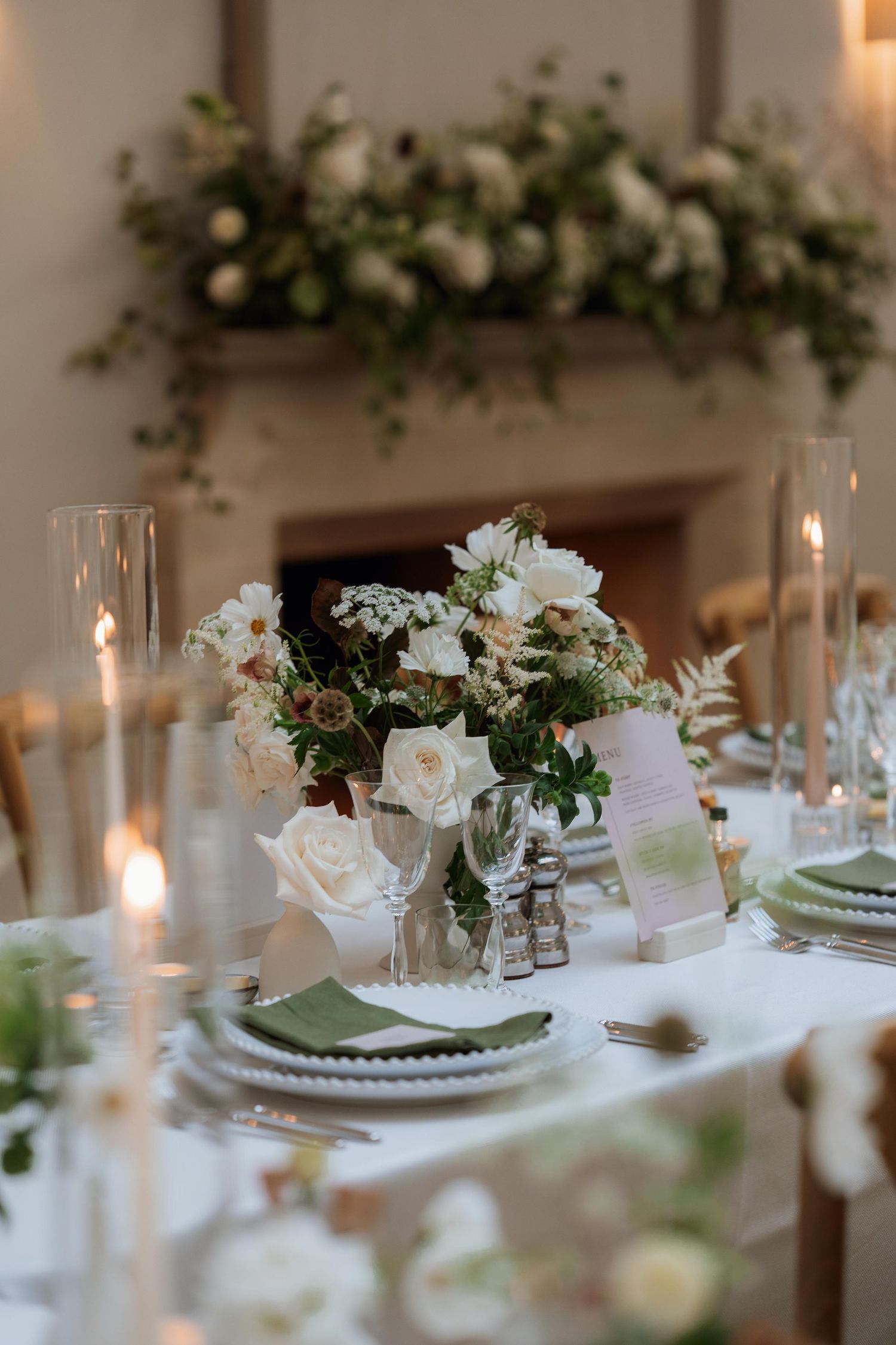 Elegant wedding table setting with white roses, greenery, and candlelight creating a romantic dining atmosphere.