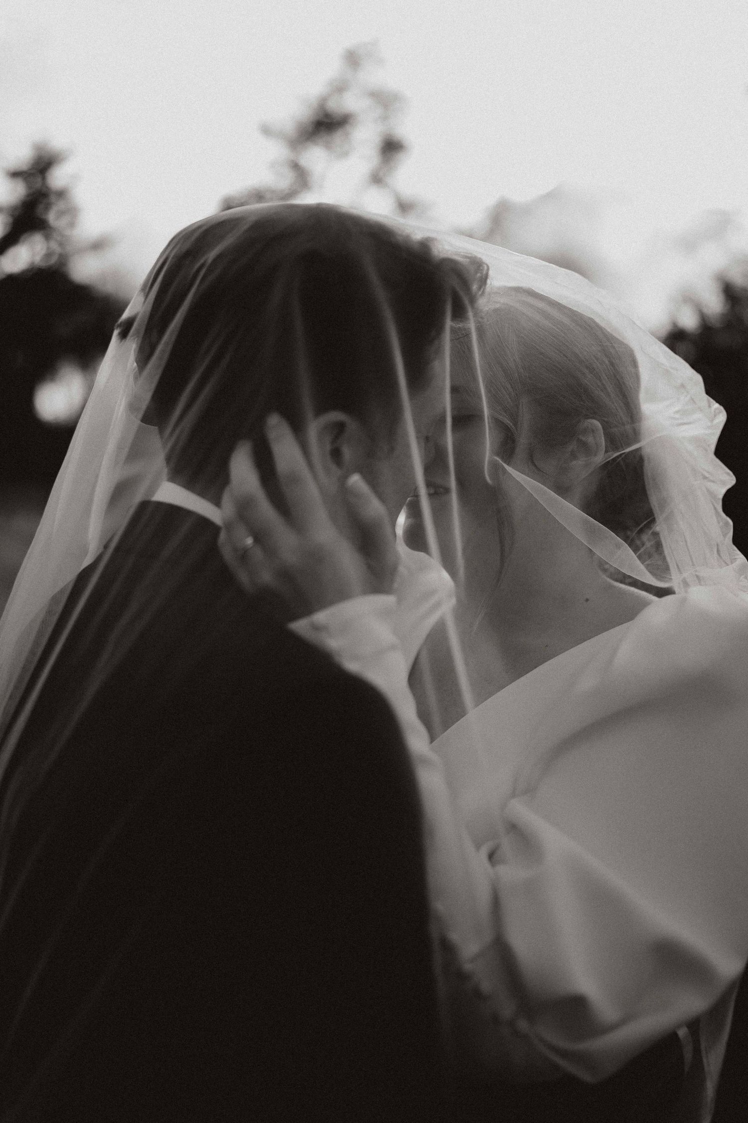 A romantic black and white wedding photo showing a tender kiss between newlyweds under a delicate white veil.