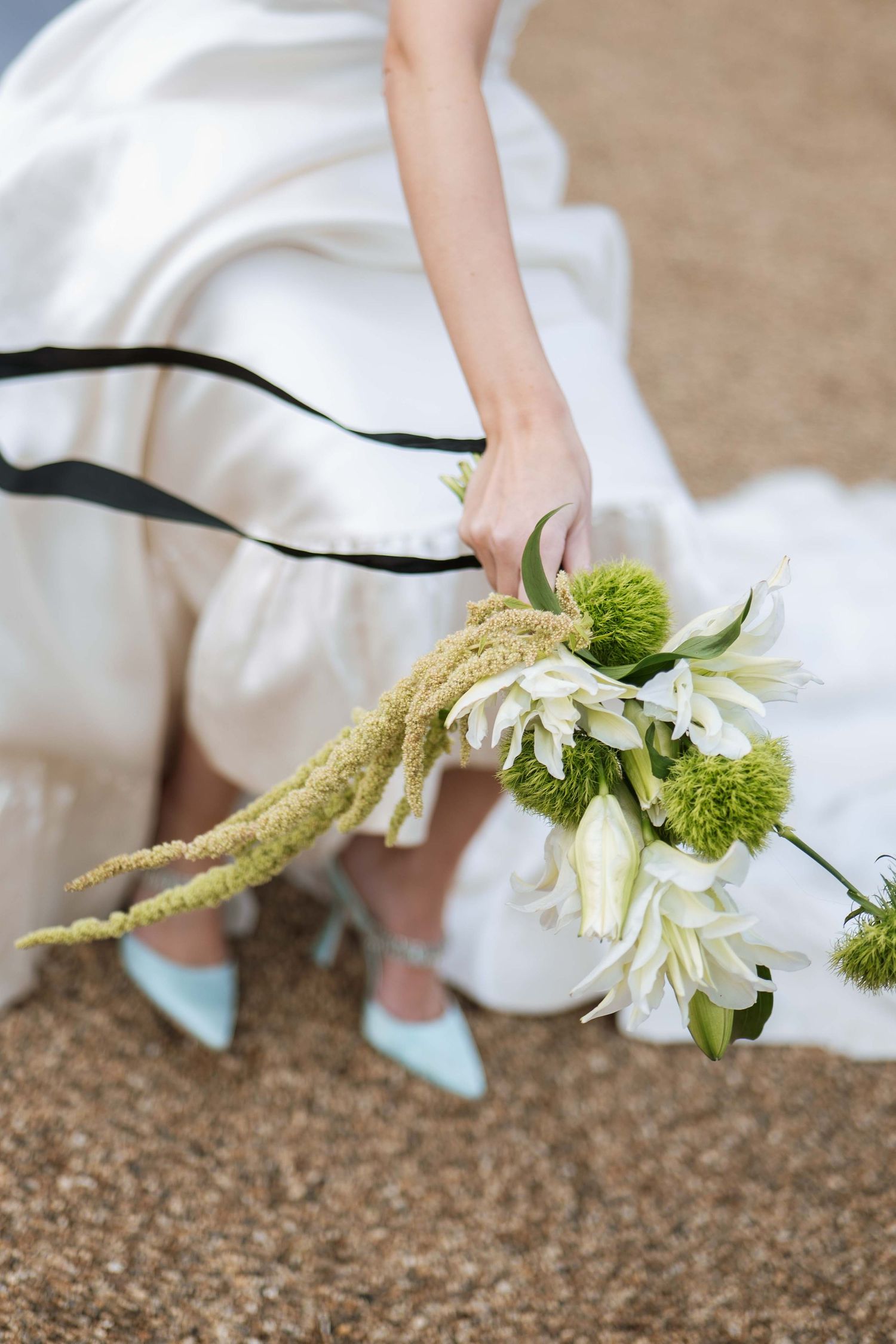A white wedding dress with turquoise shoes and a green and white floral bouquet detail against a textured ground.
