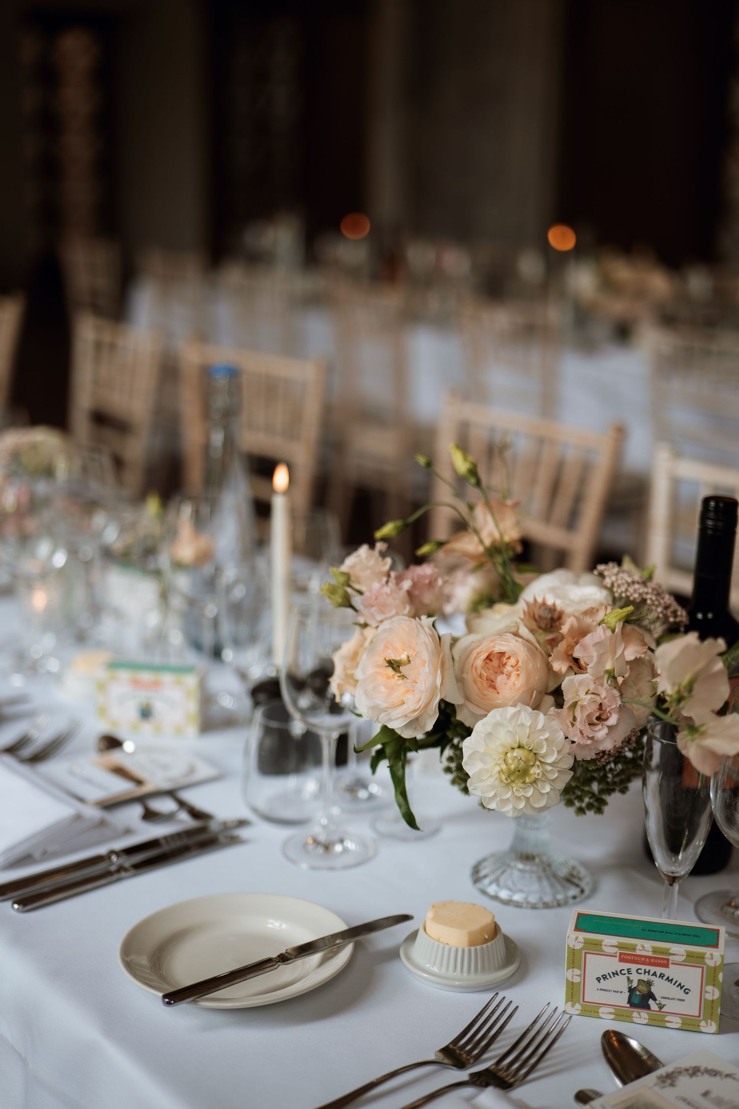 Elegant wedding table setting with blush pink roses centerpiece, white linens, wine glasses and place settings at reception.