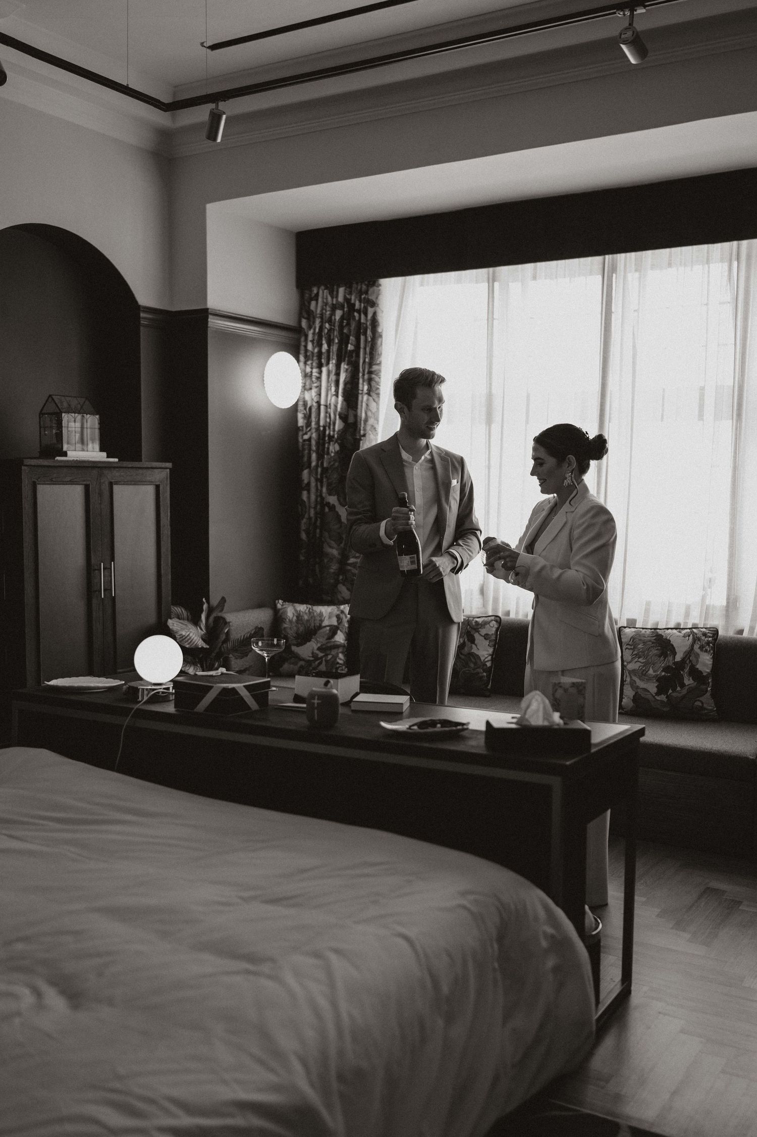 A sequence of black and white photographs showing a couple interacting in a hotel room with a bed and window.