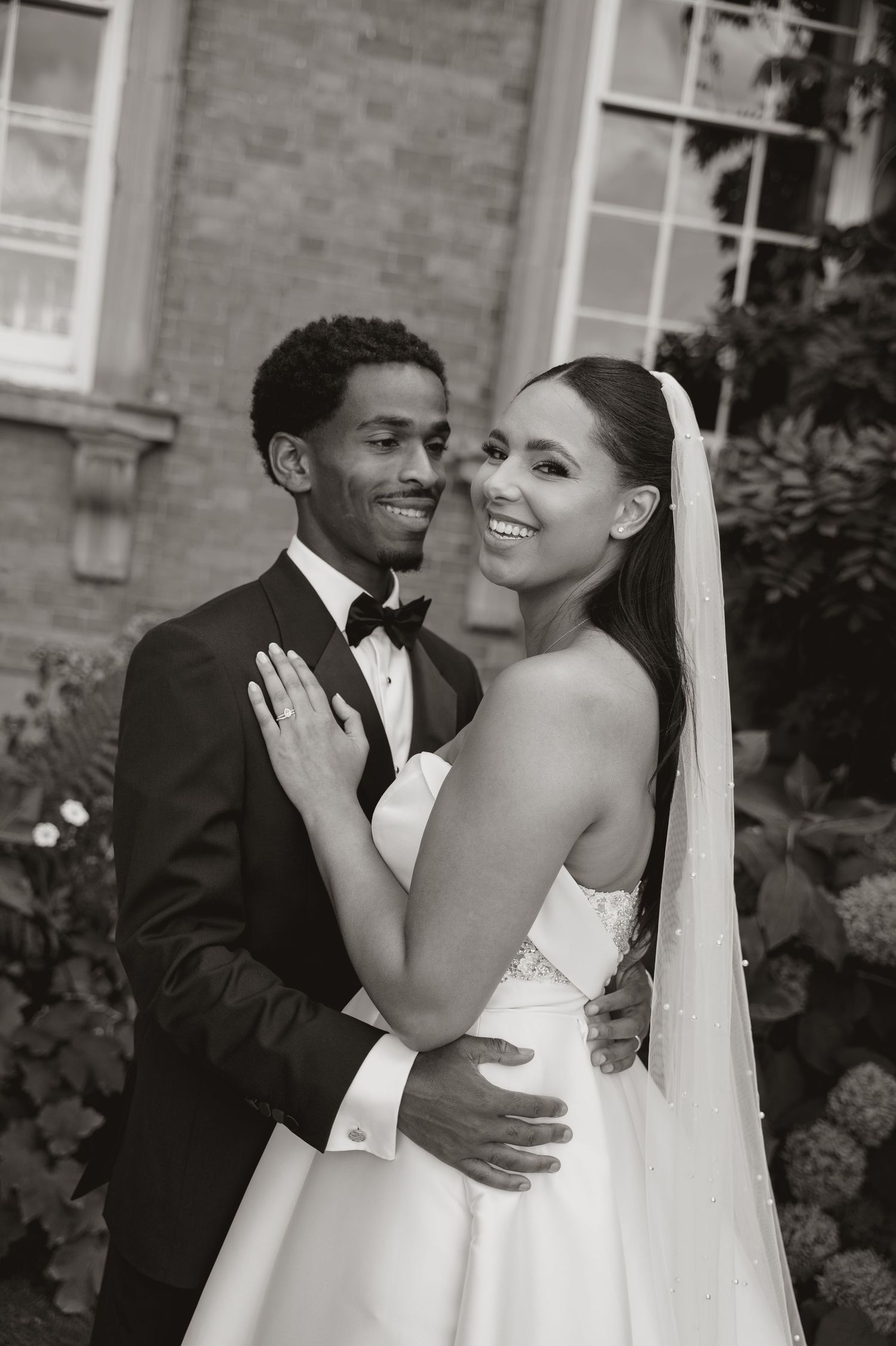A joyful bride and groom share intimate moments in a series of black and white wedding portraits outdoors.