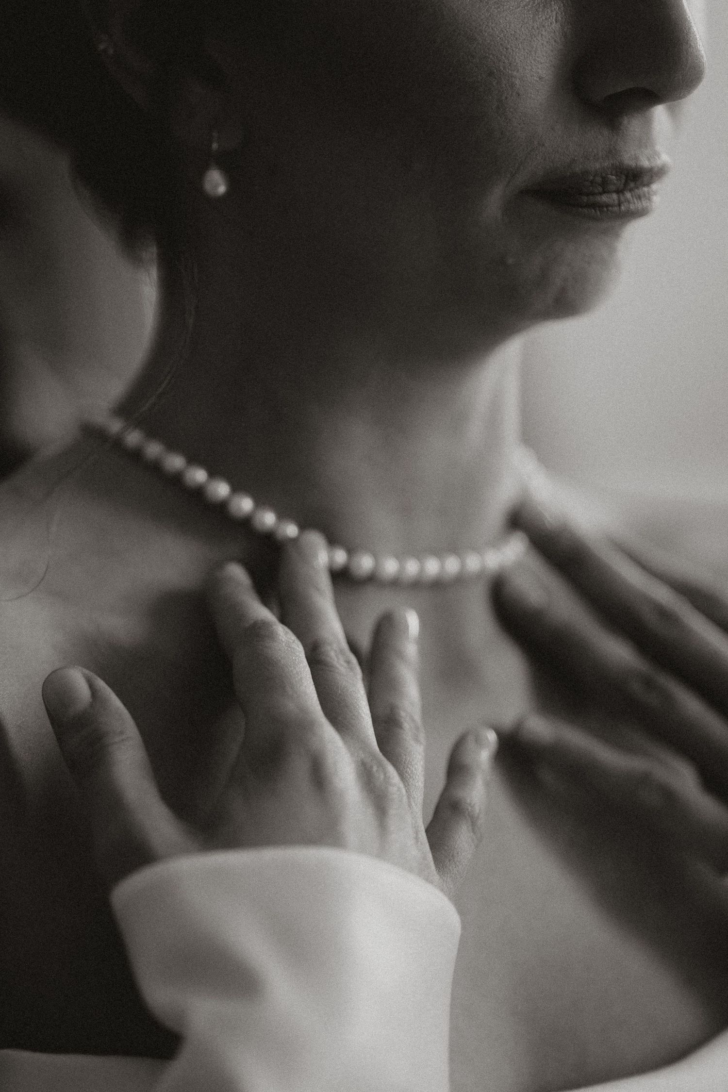 A black and white photo series showing a pearl necklace being clasped around a neck in sequential steps.