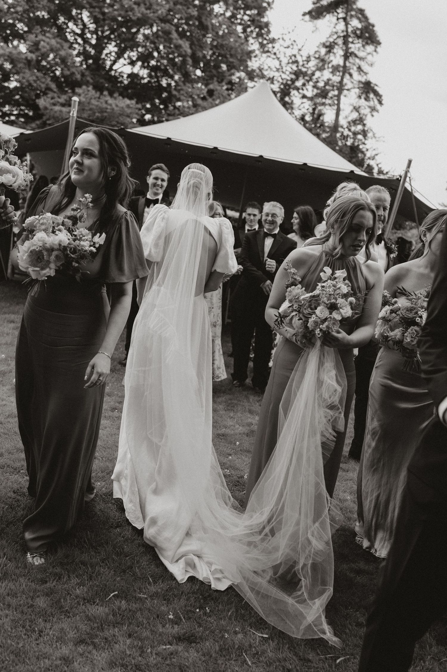 A candid sequence of black and white photos showing wedding party members in dark dresses and a flowing white gown outdoors.
