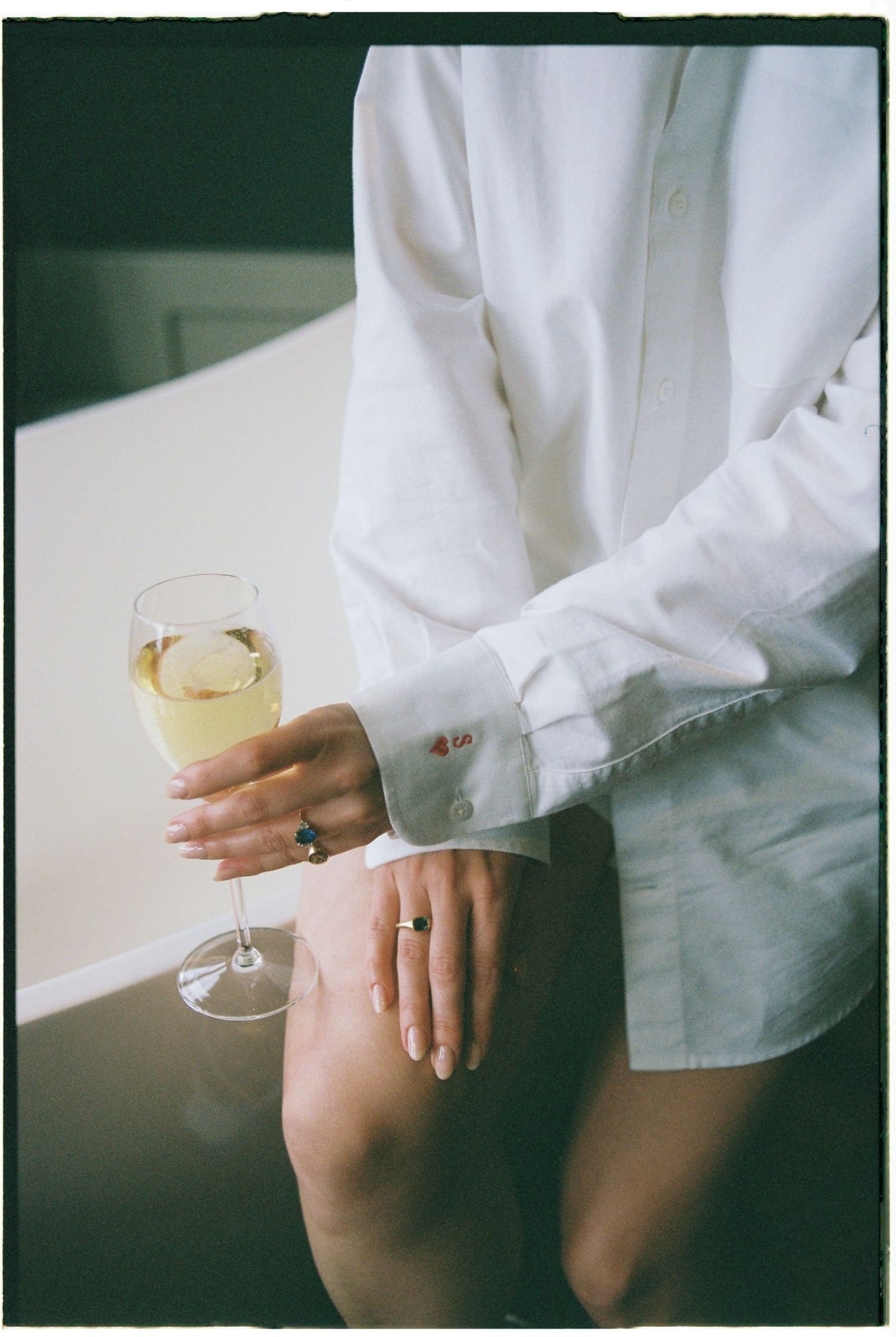 Person in white button-down shirt holding a glass of white wine while sitting on a couch.
