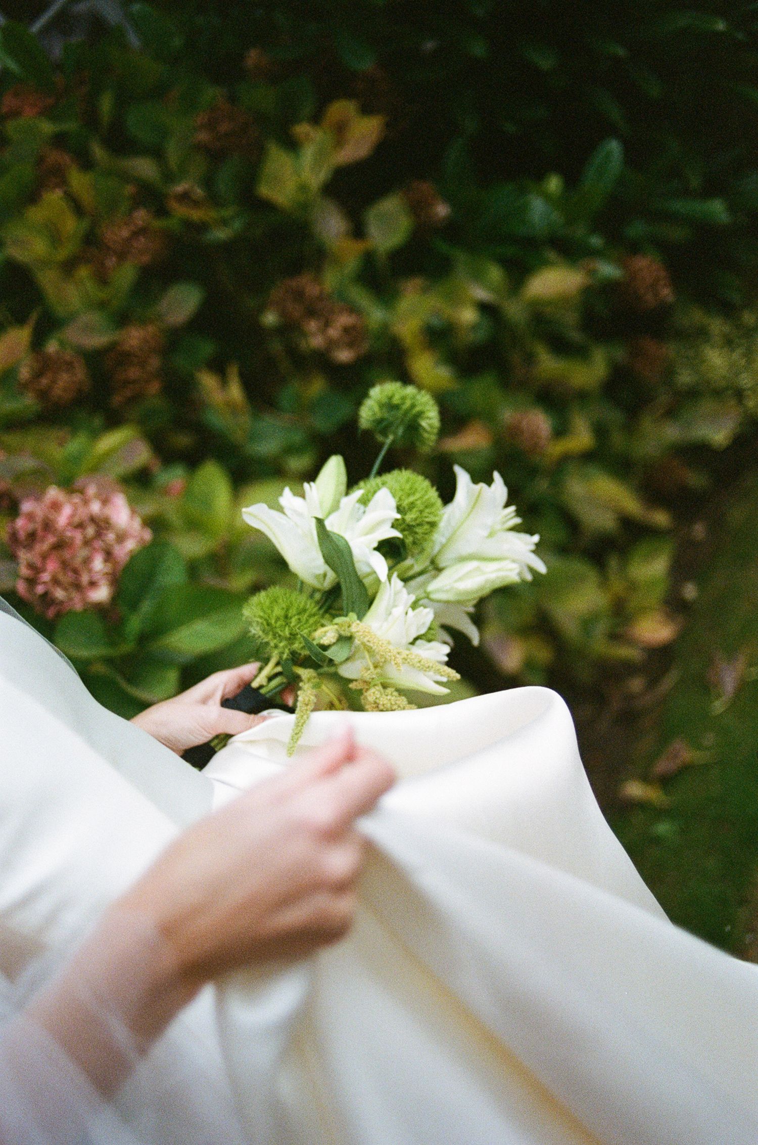 A series of white fabric swatches being held against a green garden background with flowers.