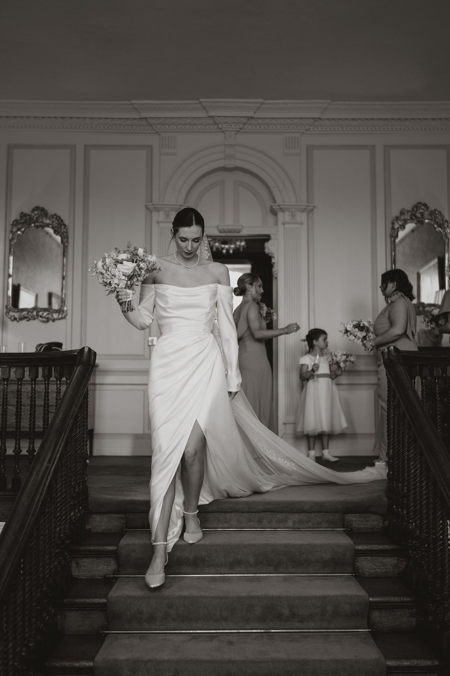 Black and white photo series shows a bride descending elegant stairs in a flowing white gown with dramatic movement.