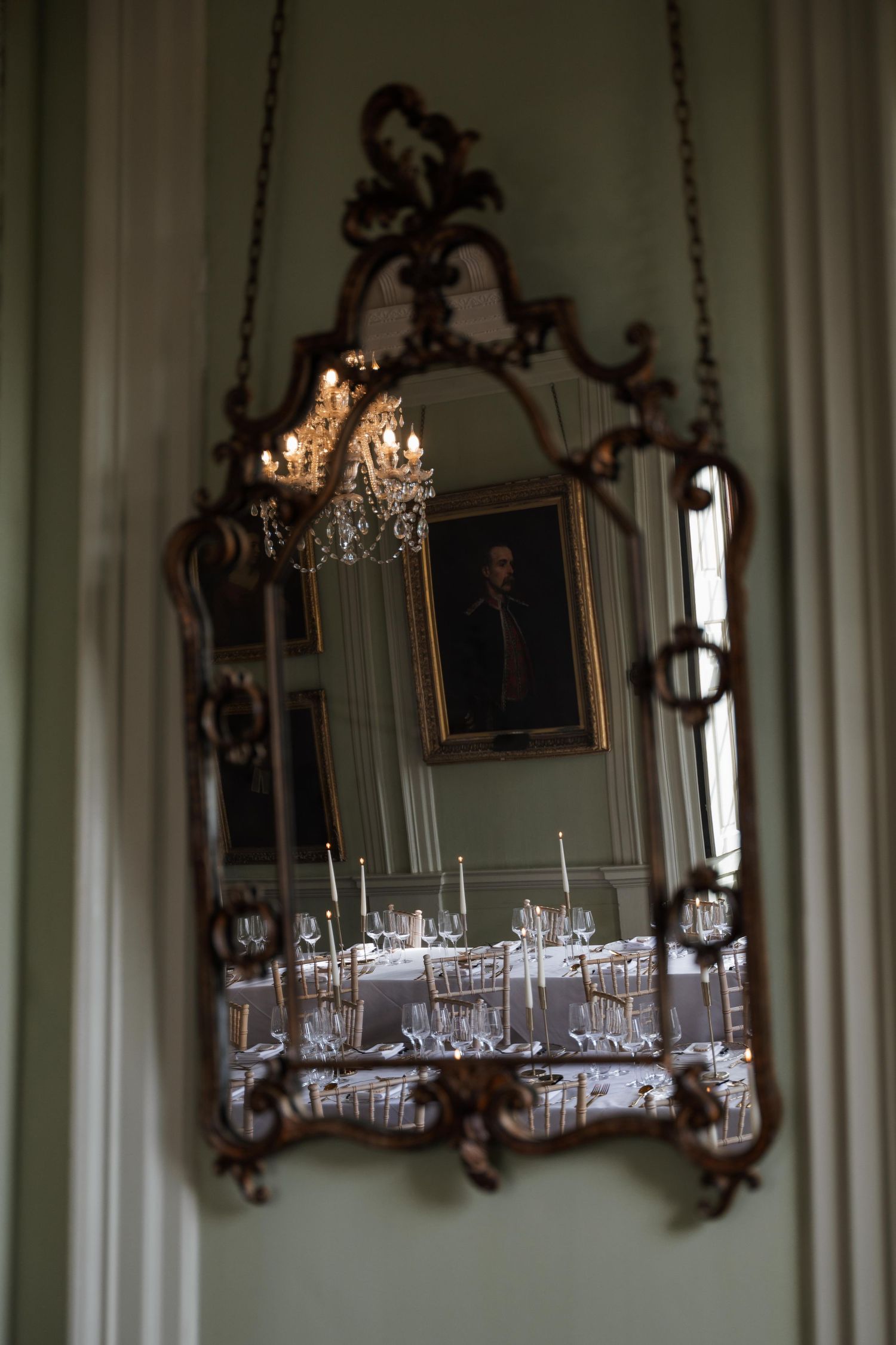 Elegant dining room with ornate gold-framed mirrors and crystal chandeliers reflecting in a classic interior setting.